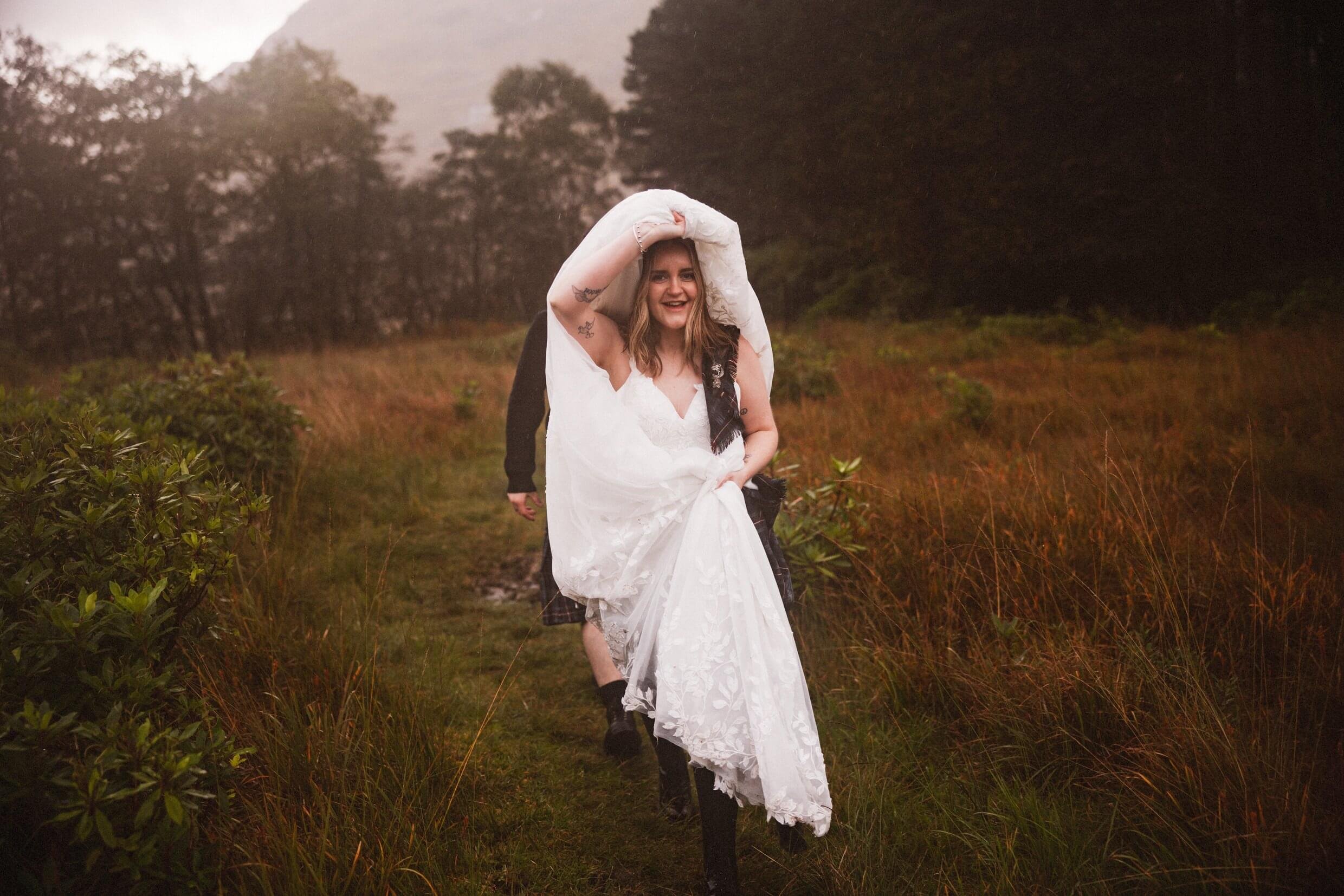 bride uses dress to cover hair during wet glencoe elopement in glen etive scotland