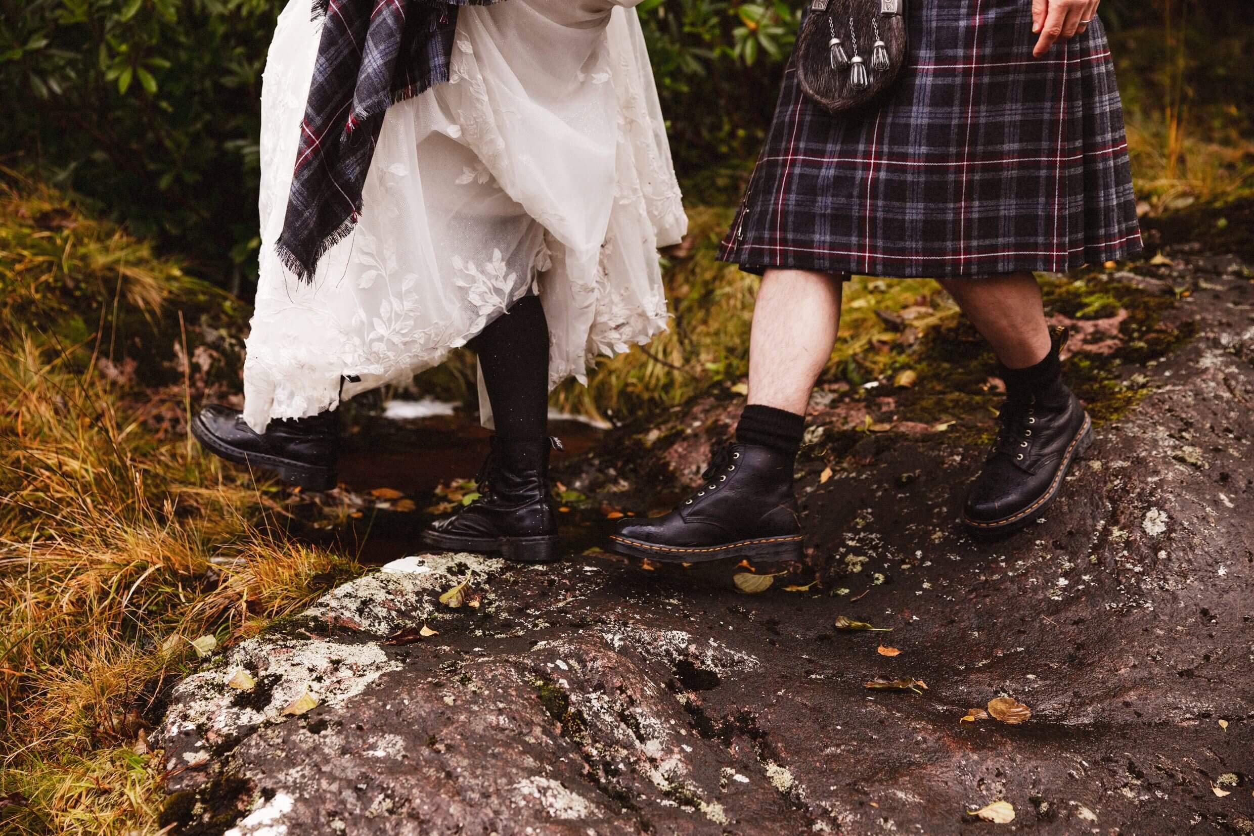 bride and groom wearing boots climb over rocks during glencoe elopement in glen etive scotland