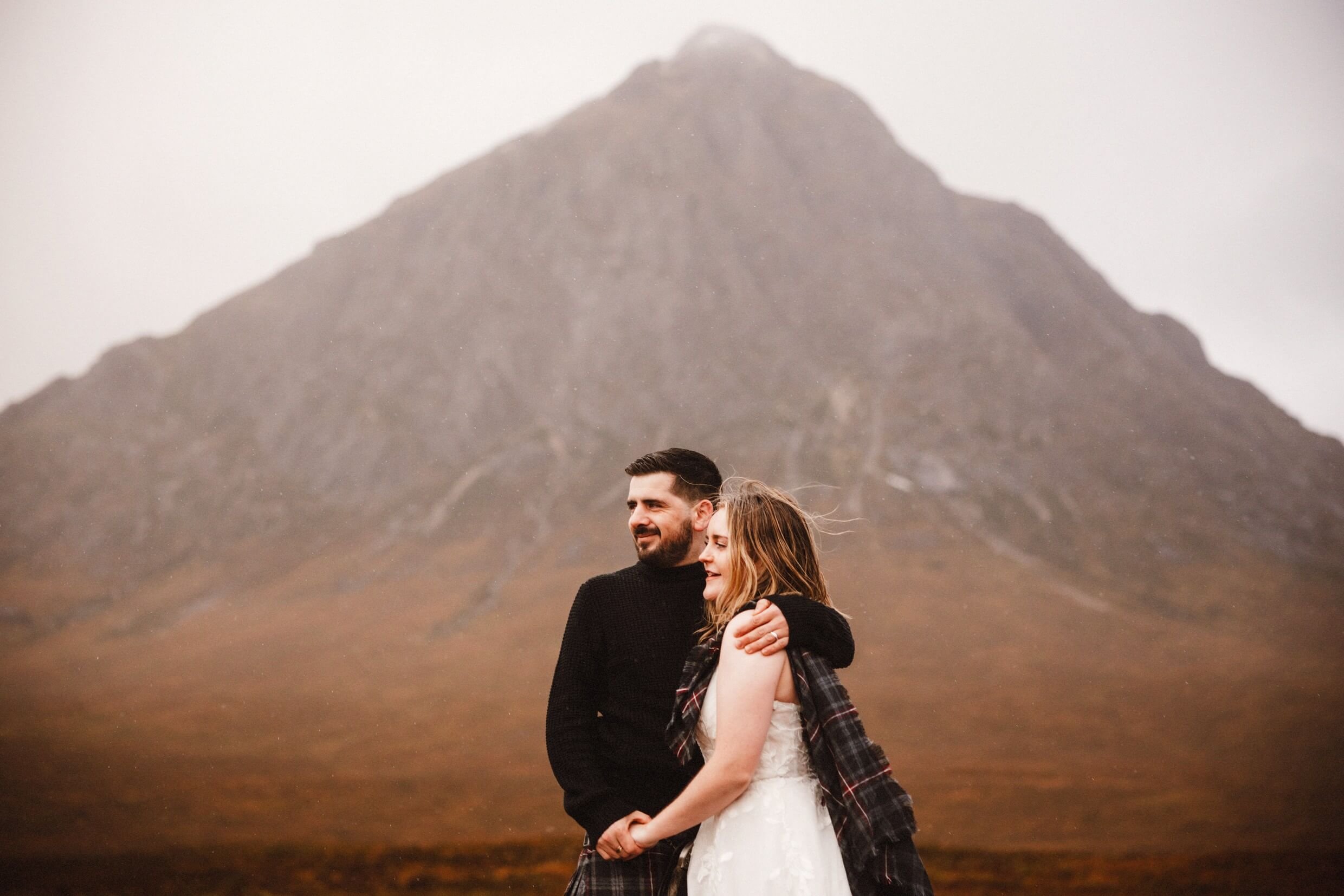 bride and groom looking into the distance in glencoe scotland with a mountain in the background 