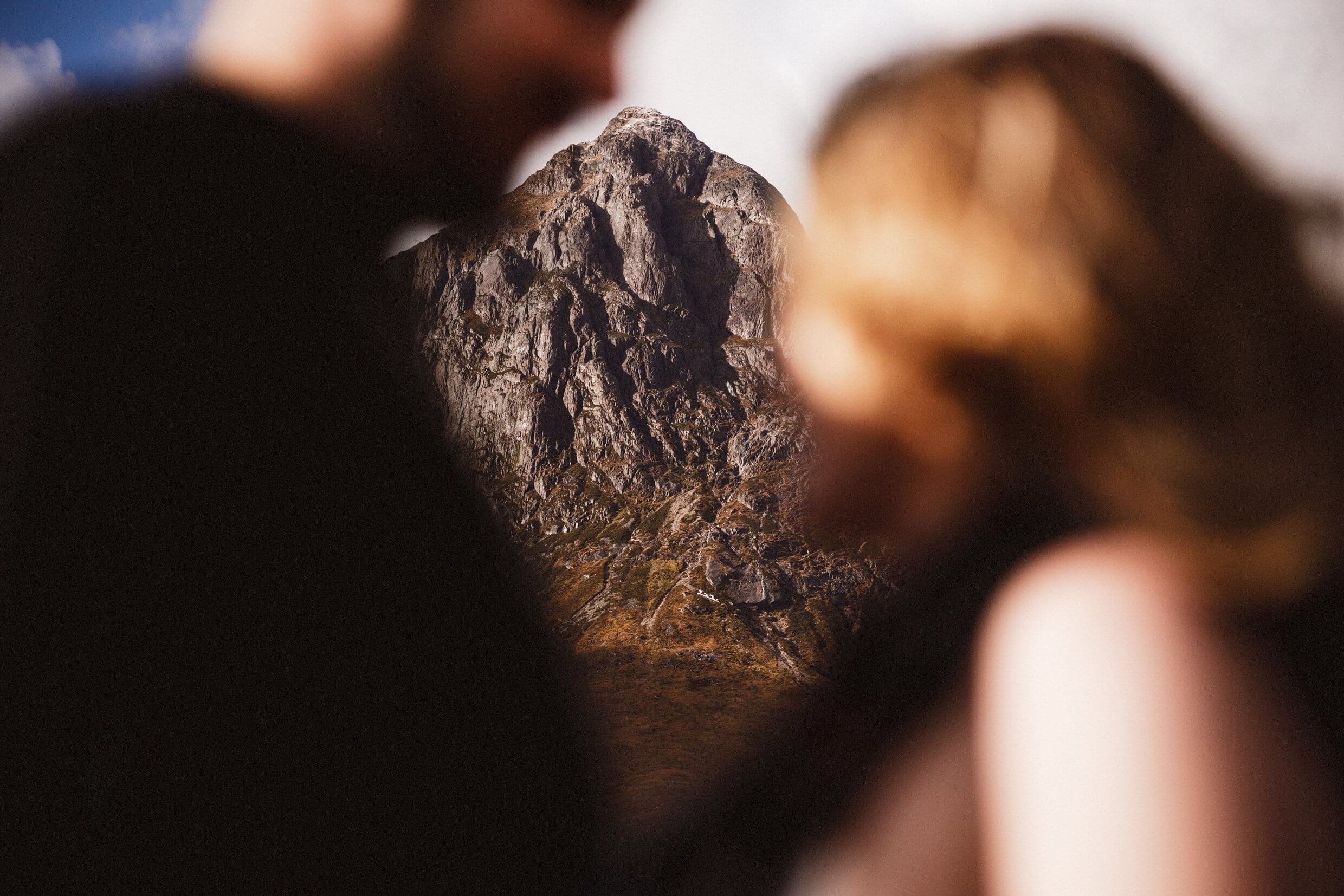 bride and groom in foreground and out of focus framing a sunlit mountain during glencoe elopement