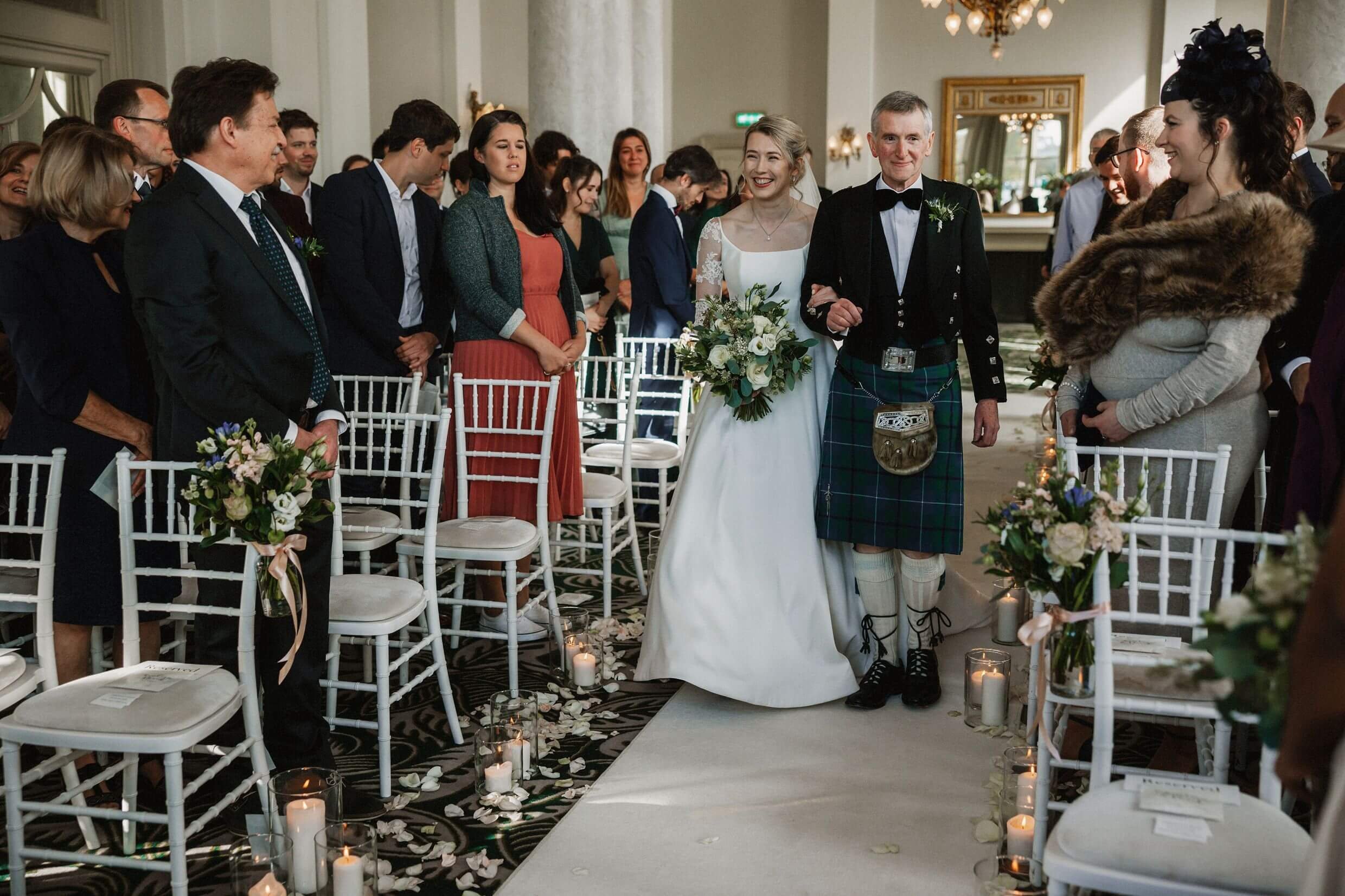 the bride and father of the bride walk up the aisle as guests look on during balmoral hotel edinburgh wedding ceremony in scotland