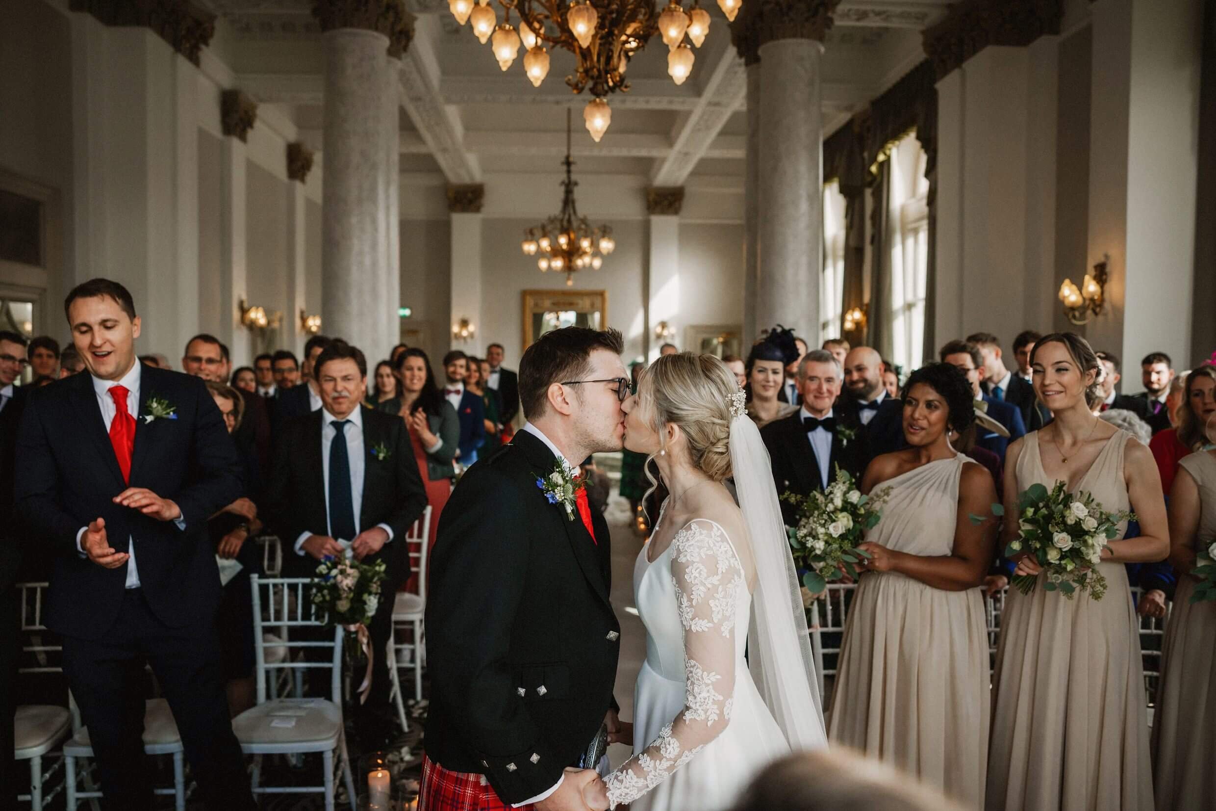 the bride and groom kiss following their balmoral hotel edinburgh wedding ceremony as wedding guests look on