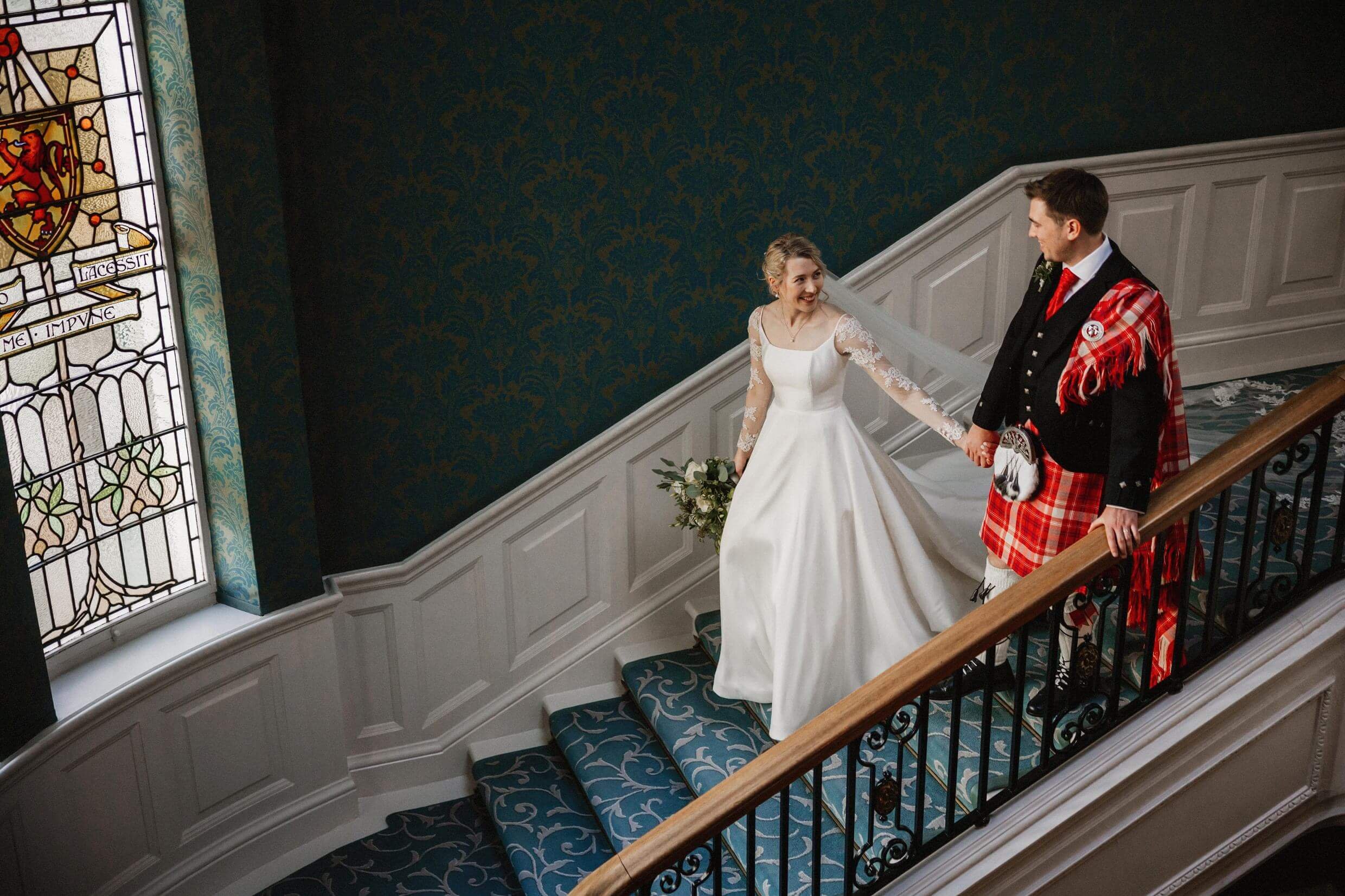 the bride and groom walk down a staircase at the balmoral hotel edinburgh wedding venue in scotland