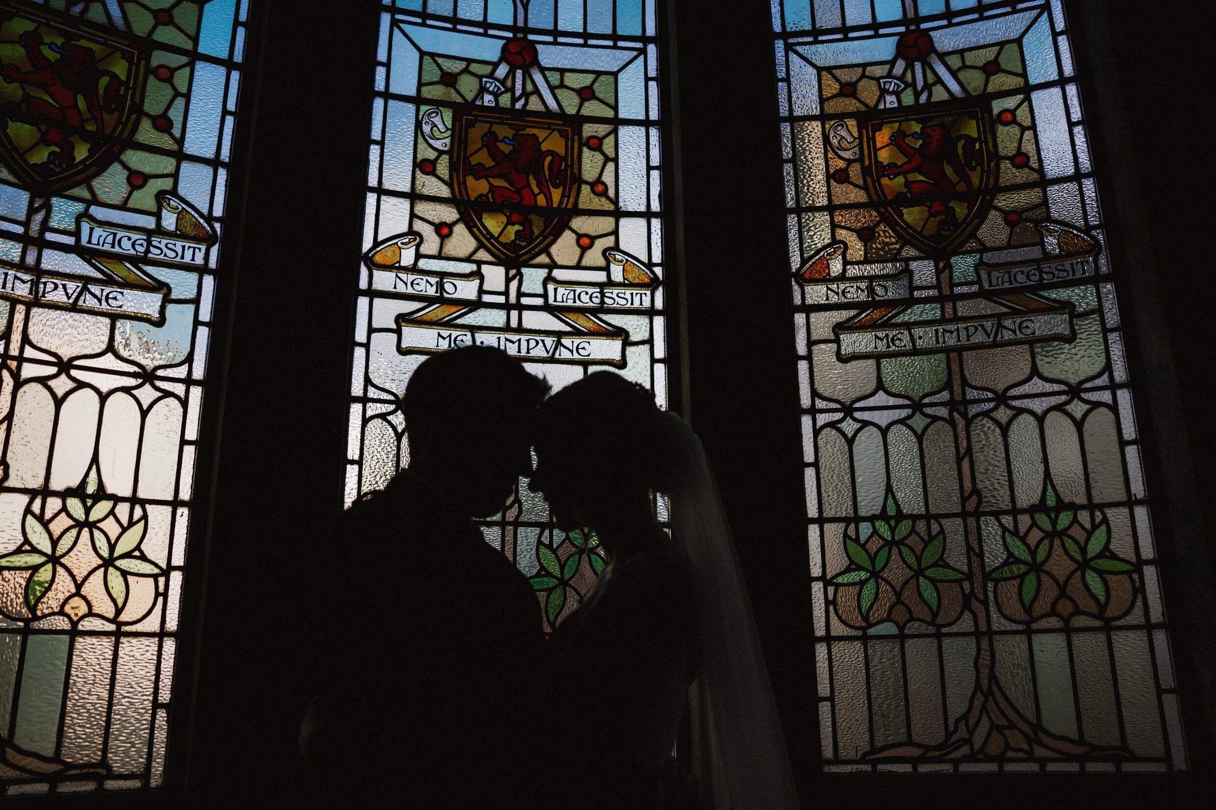 the bride and groom embrace in front of a stained glass window at the balmoral hotel edinburgh wedding venue in scotland