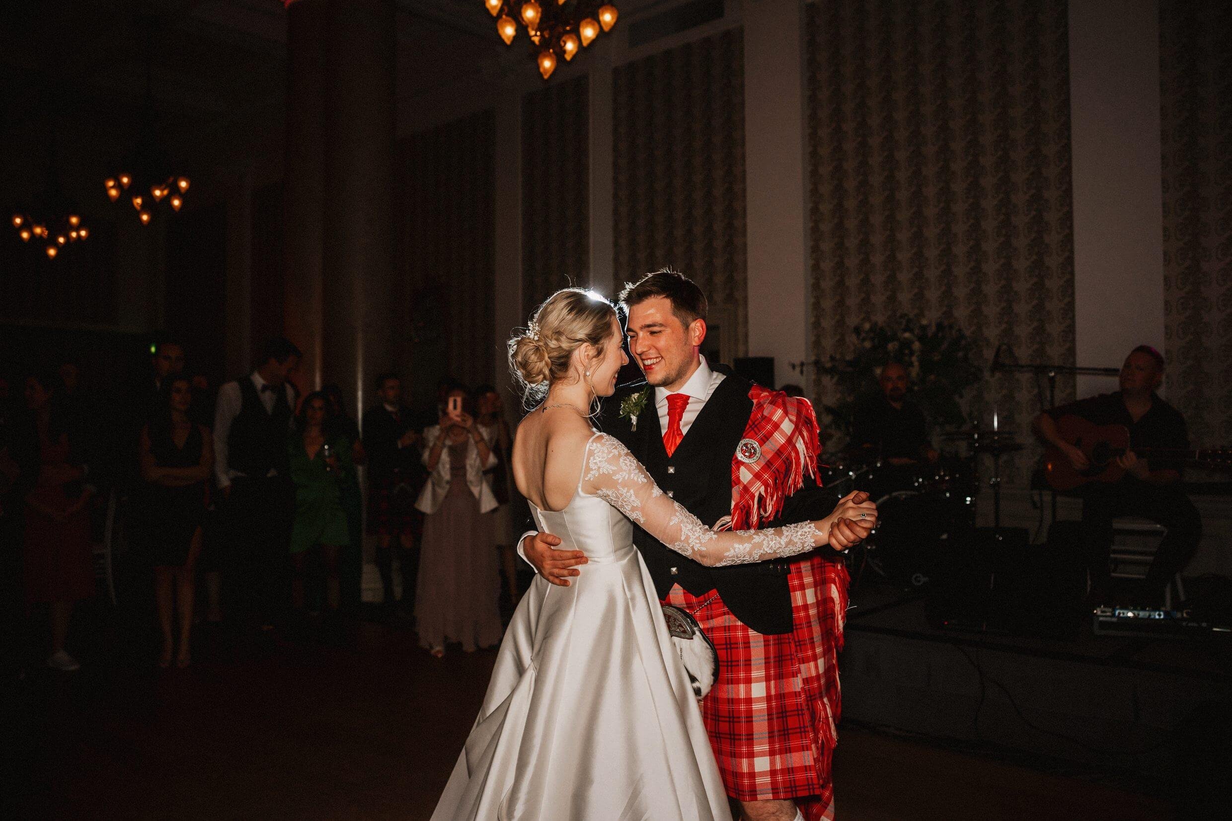 the bride and groom's first dance at the balmoral hotel edinburgh wedding venue in scotland with the band visible in the background