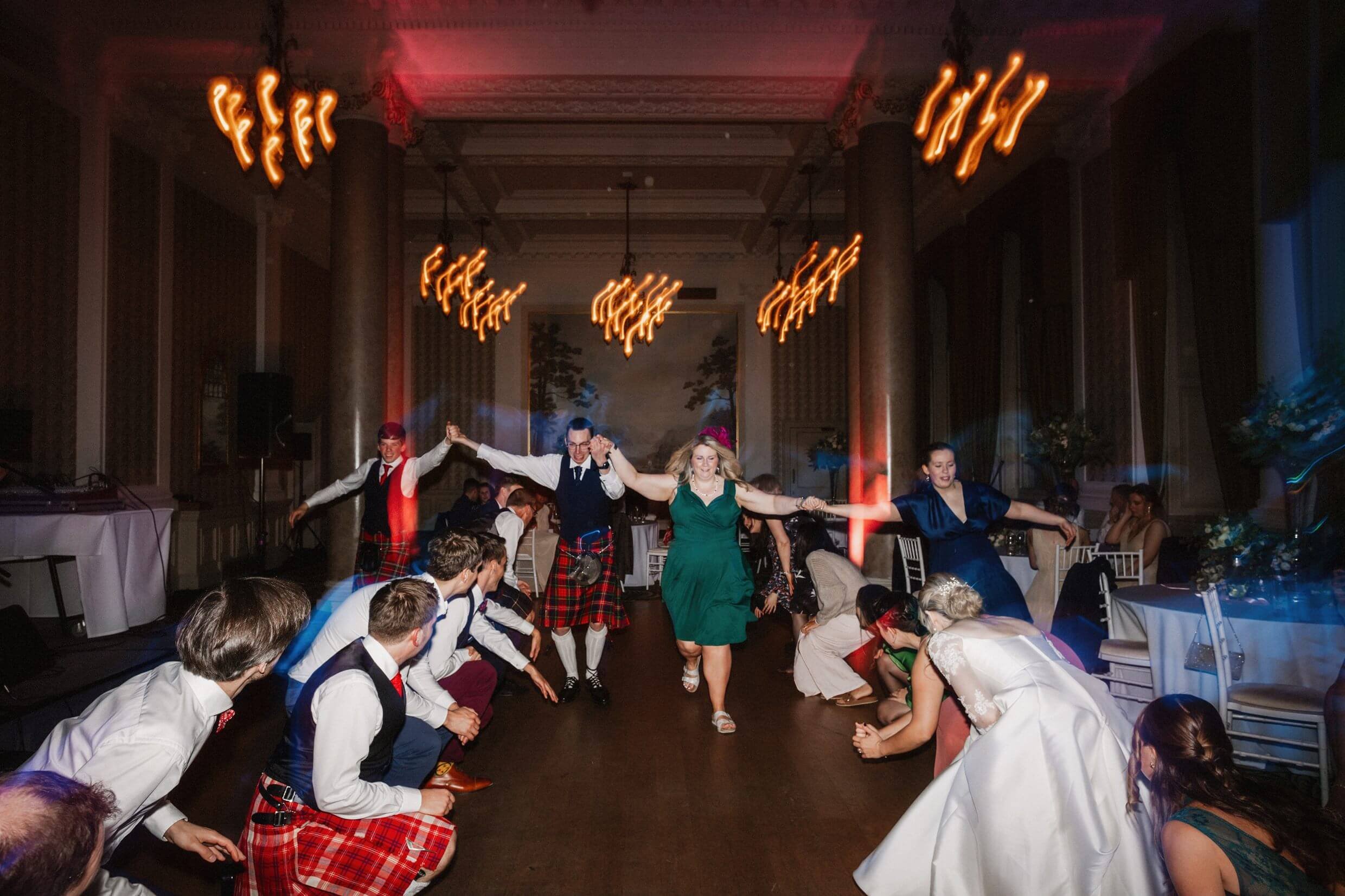 the wedding party ceilidh dancing beneath chandeliers at the balmoral hotel edinburgh wedding venue in scotland