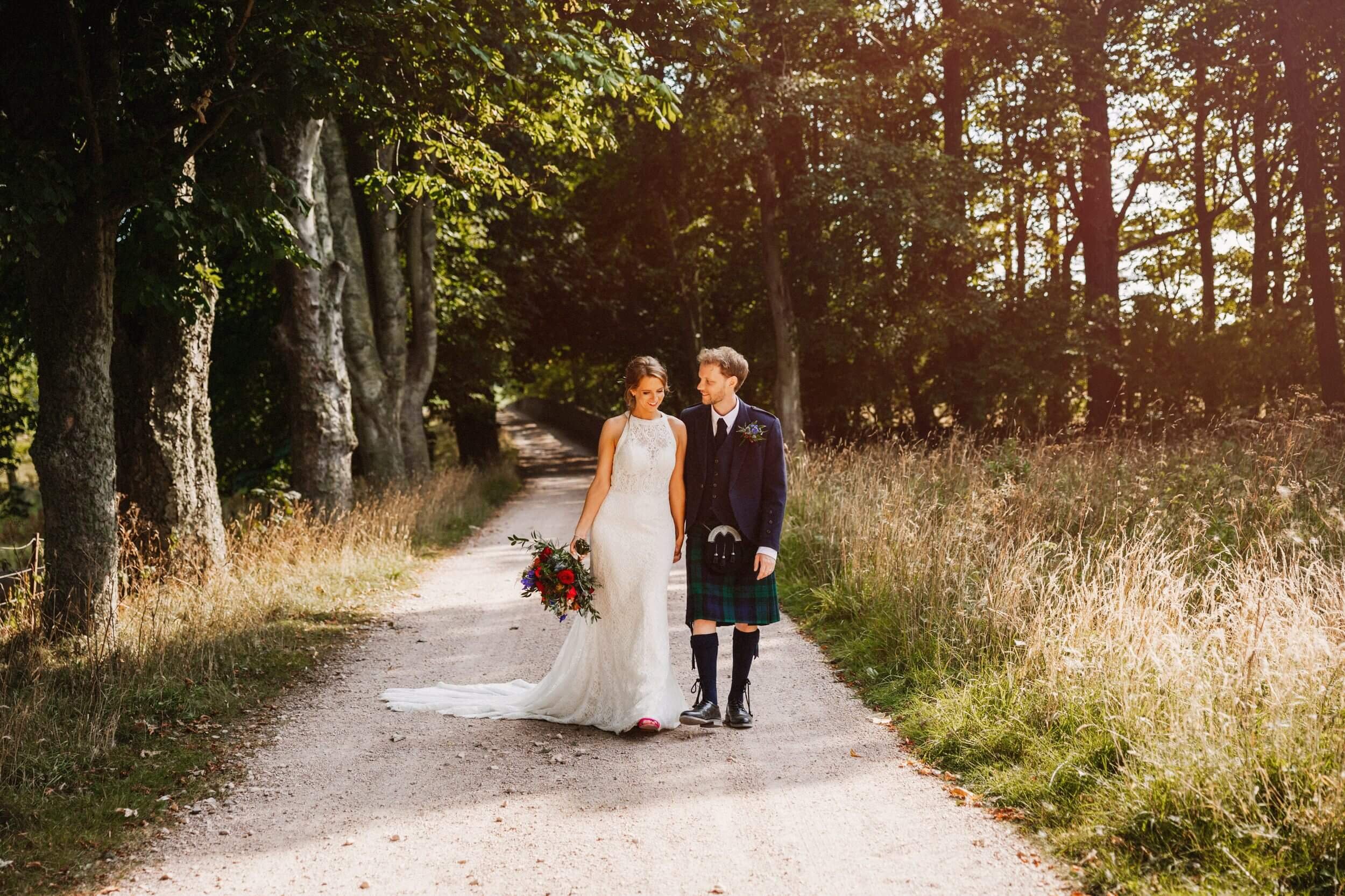 glasgow wedding photographer shoots a bride and groom walking hand in hand along a woodland path with trees on either side