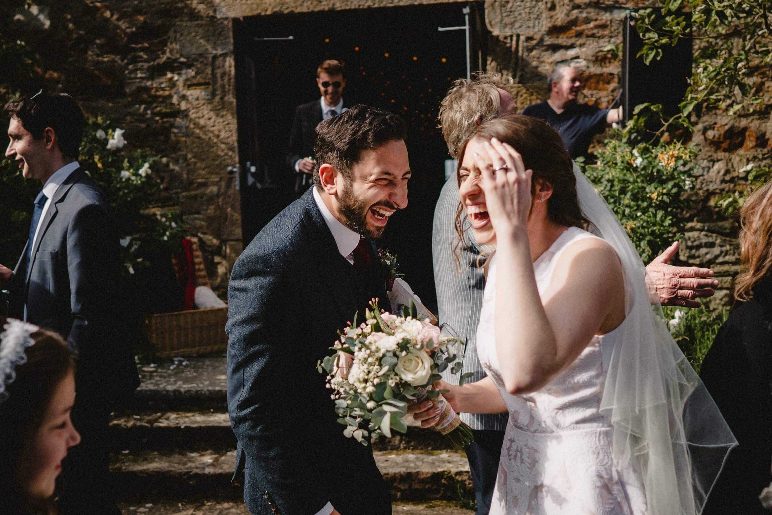 the bride and groom laugh together standing in front of a building with stone steps captured by a glasgow wedding photographer