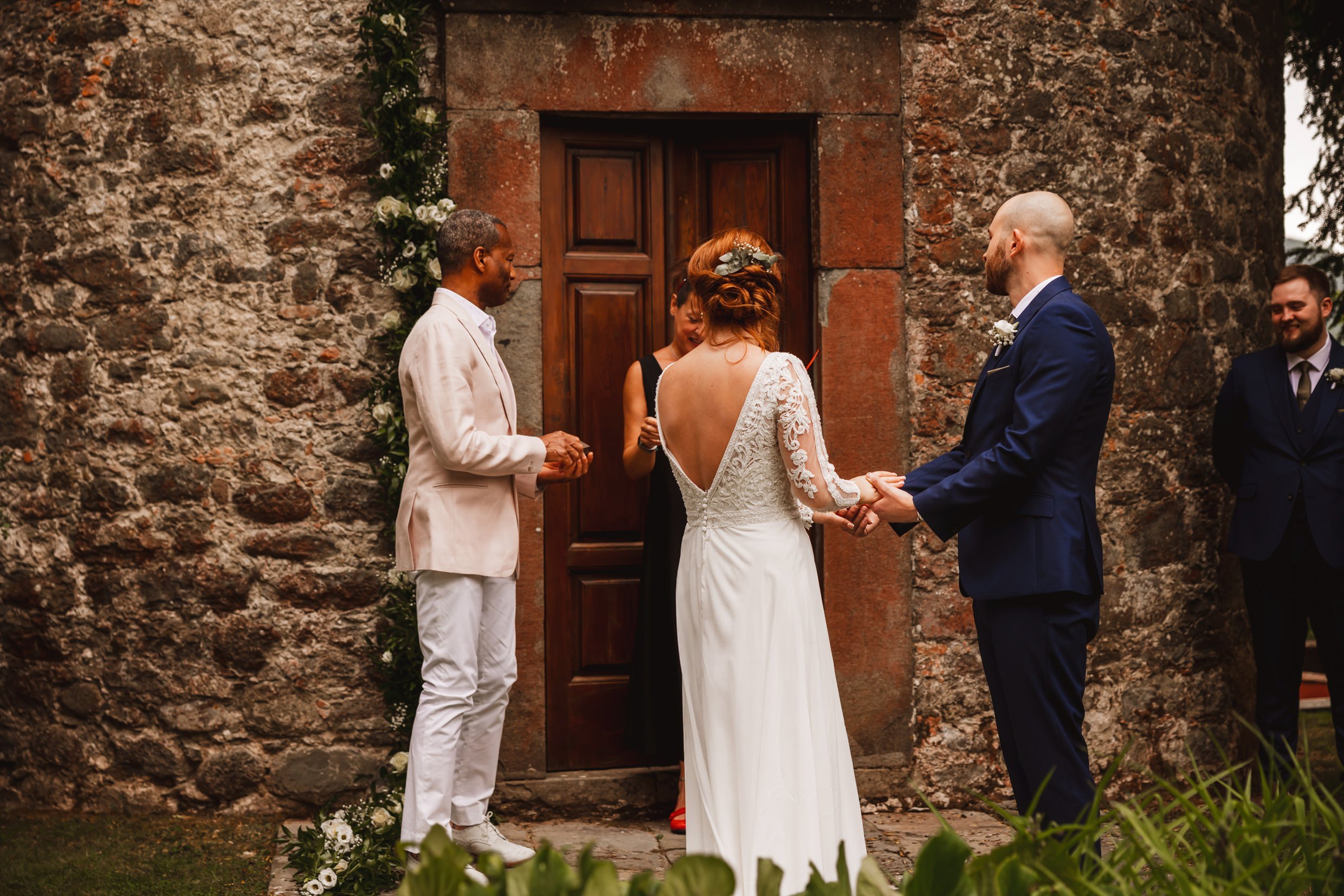 the bride and groom hold hands during wedding ceremony outside the private chapel at the agriturismo la torre italian destination wedding venue in bagni di lucca tuscany
