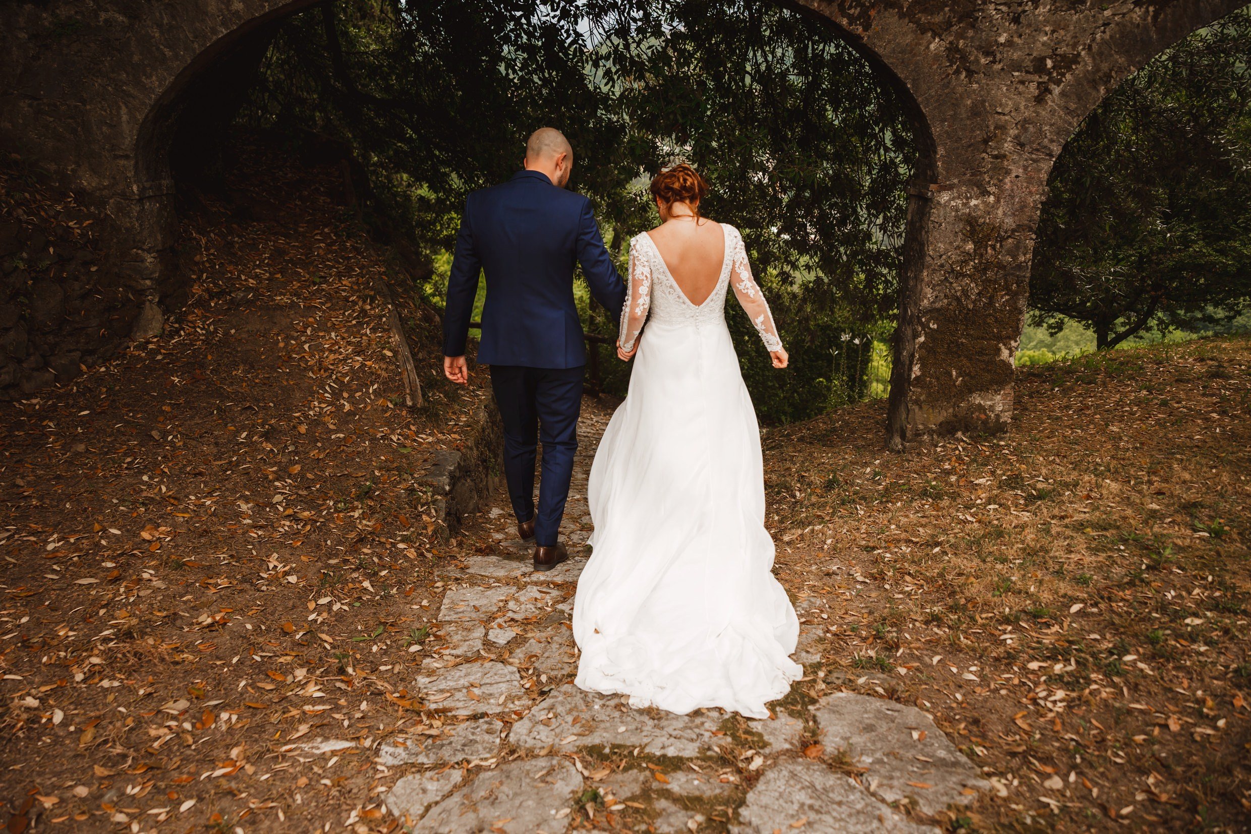 the bride and groom walk through a stone archway following their wedding ceremony at the agriturismo la torre italian destination wedding venue in bagni di lucca tuscany