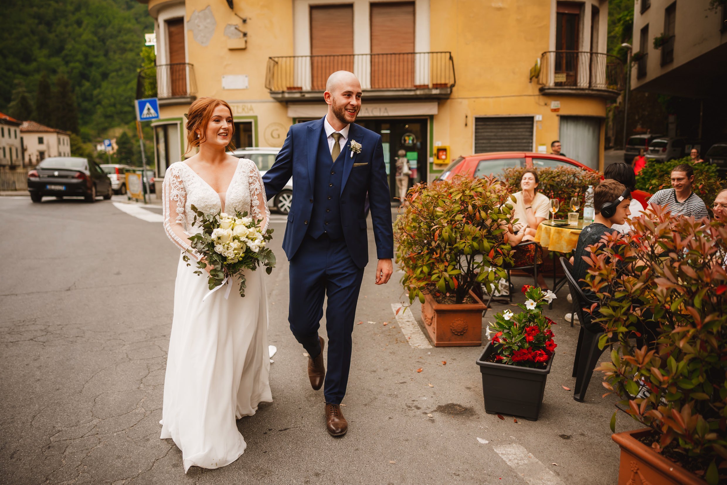 bride and groom walking past a cafe in bagni di lucca in tuscany during their italian destination wedding