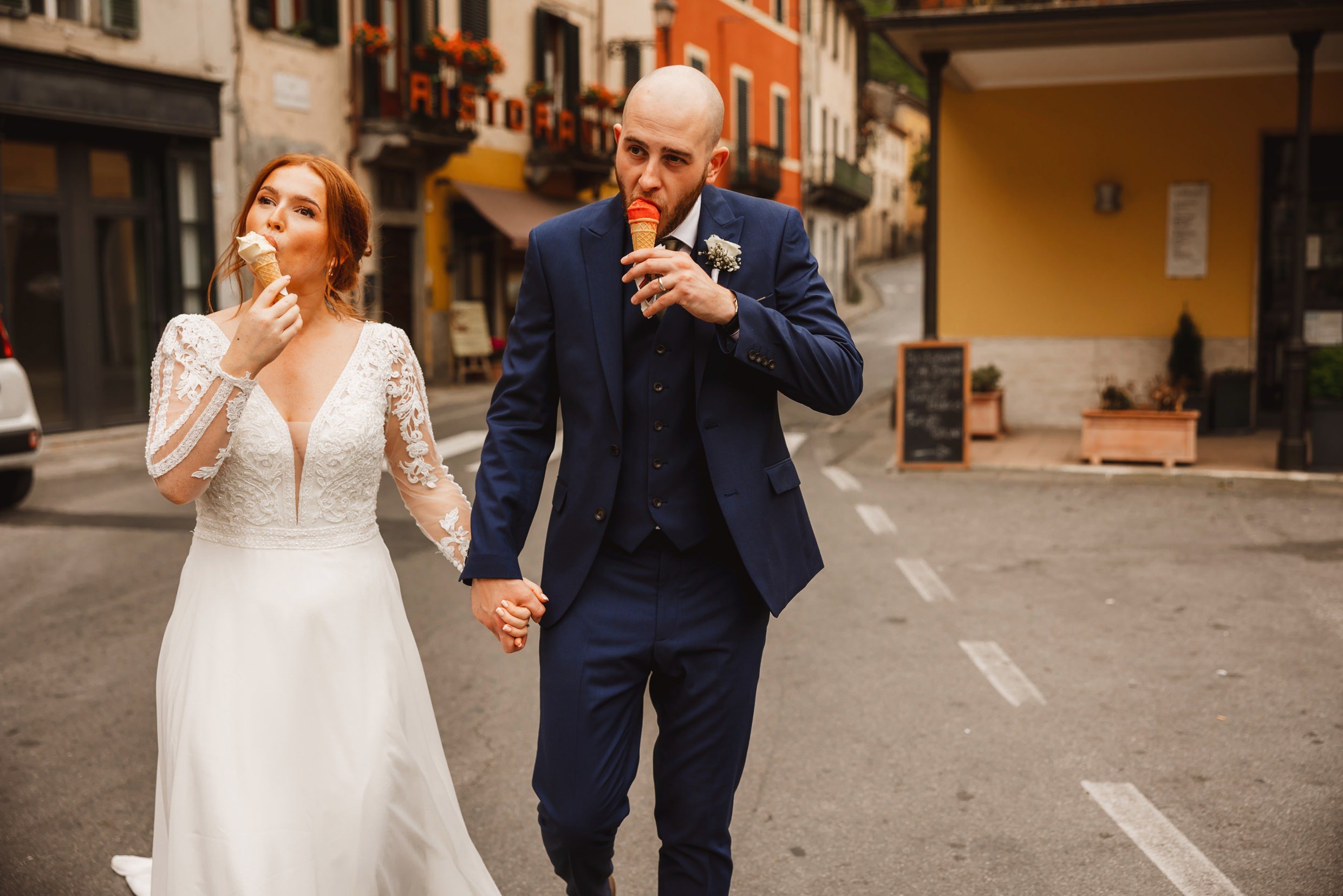 bride and groom eat ice cream cones while walking in bagni di lucca in tuscany during their italian destination wedding