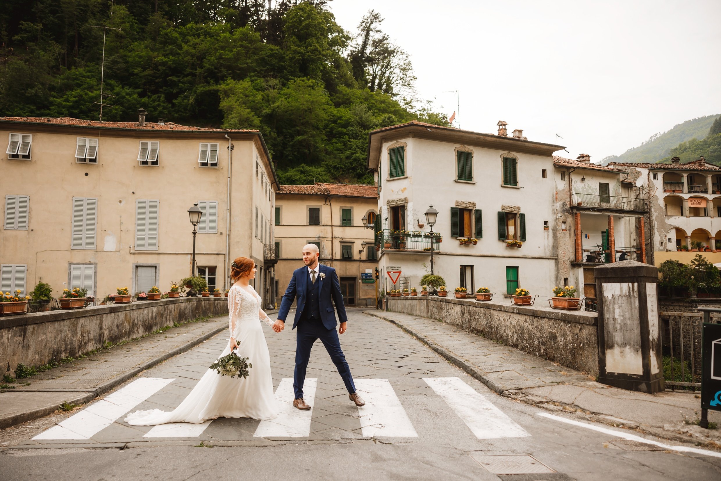 the bride and groom hold hands while walking through bagni di lucca in tuscany during their italian destination wedding