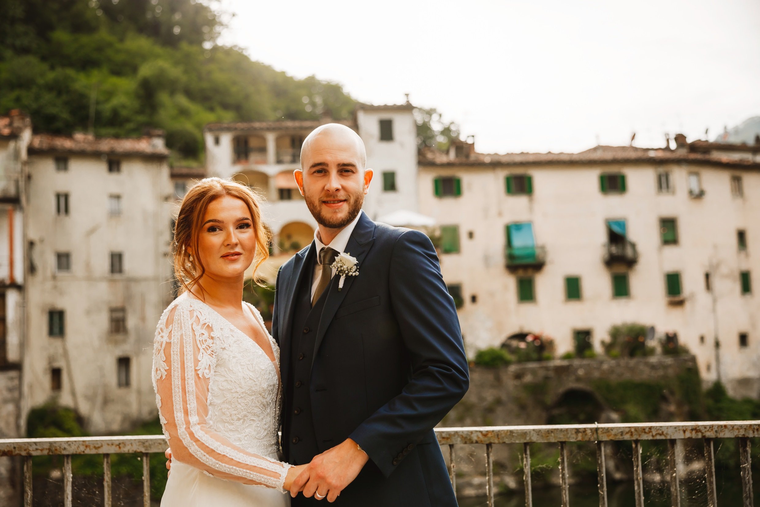 the bride and groom standing in front of old buildings in bagni di lucca in tuscany during their italian destination wedding