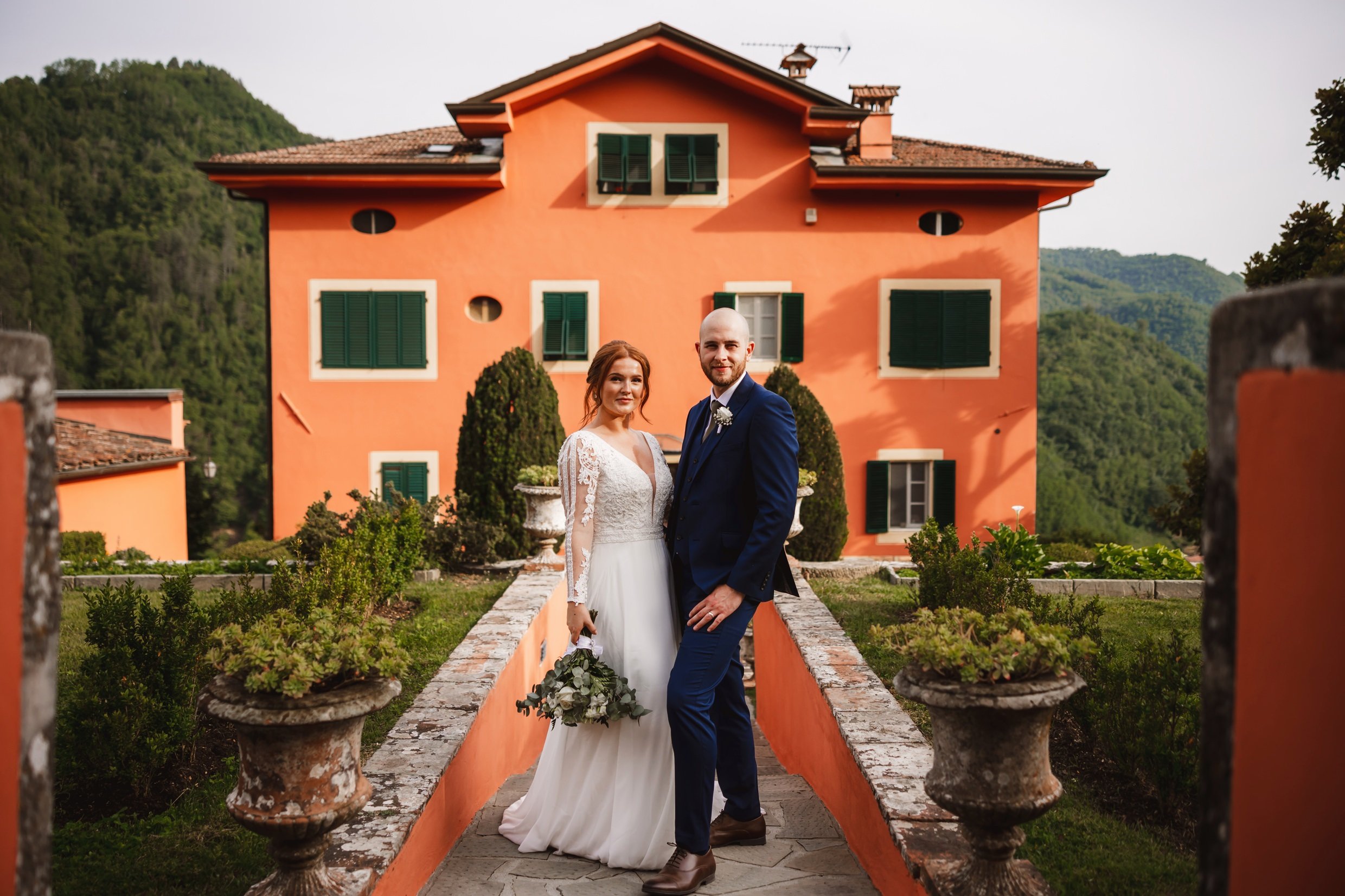 the bride and groom standing in front of a villa at the agriturismo la torre italian destination wedding venue in bagni di lucca tuscany