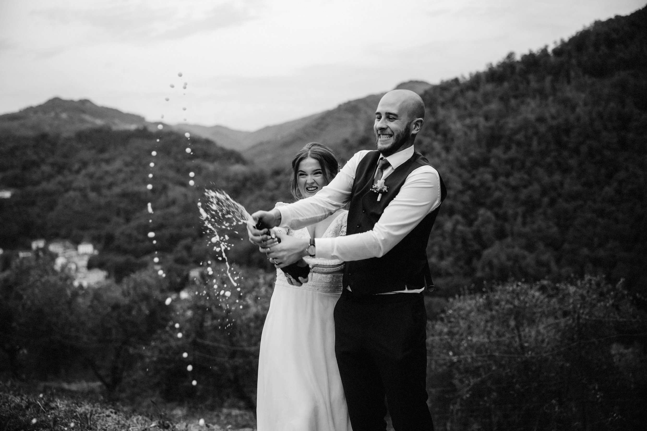 the bride and groom spray champagne with hills and trees in the background at the agriturismo la torre italian destination wedding venue in bagni di lucca tuscany