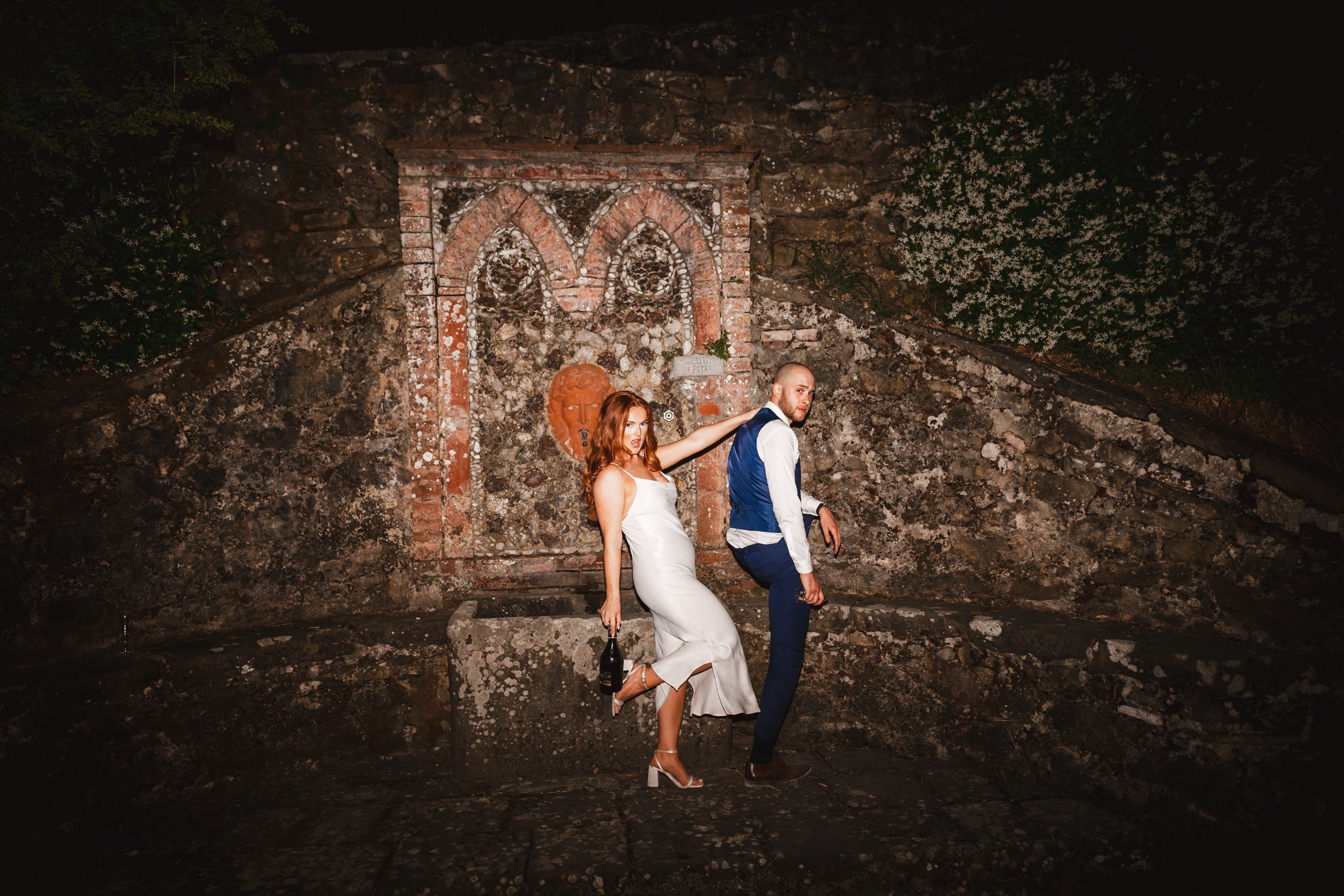 the bride and groom pose for photographs at night outside at the agriturismo la torre italian destination wedding venue in bagni di lucca tuscany