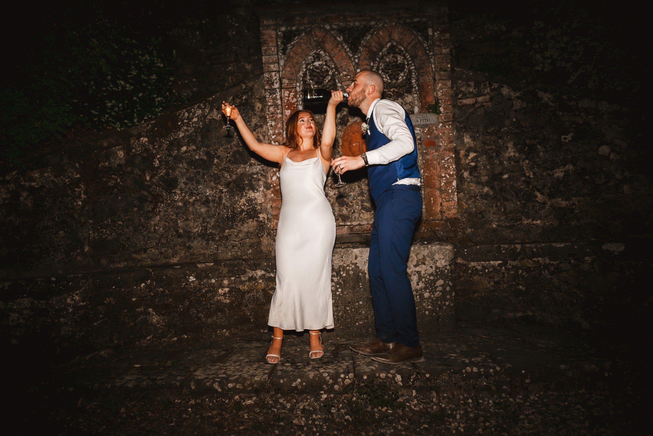 the bride and groom pose for photographs at night outside at the agriturismo la torre italian destination wedding venue in bagni di lucca tuscany