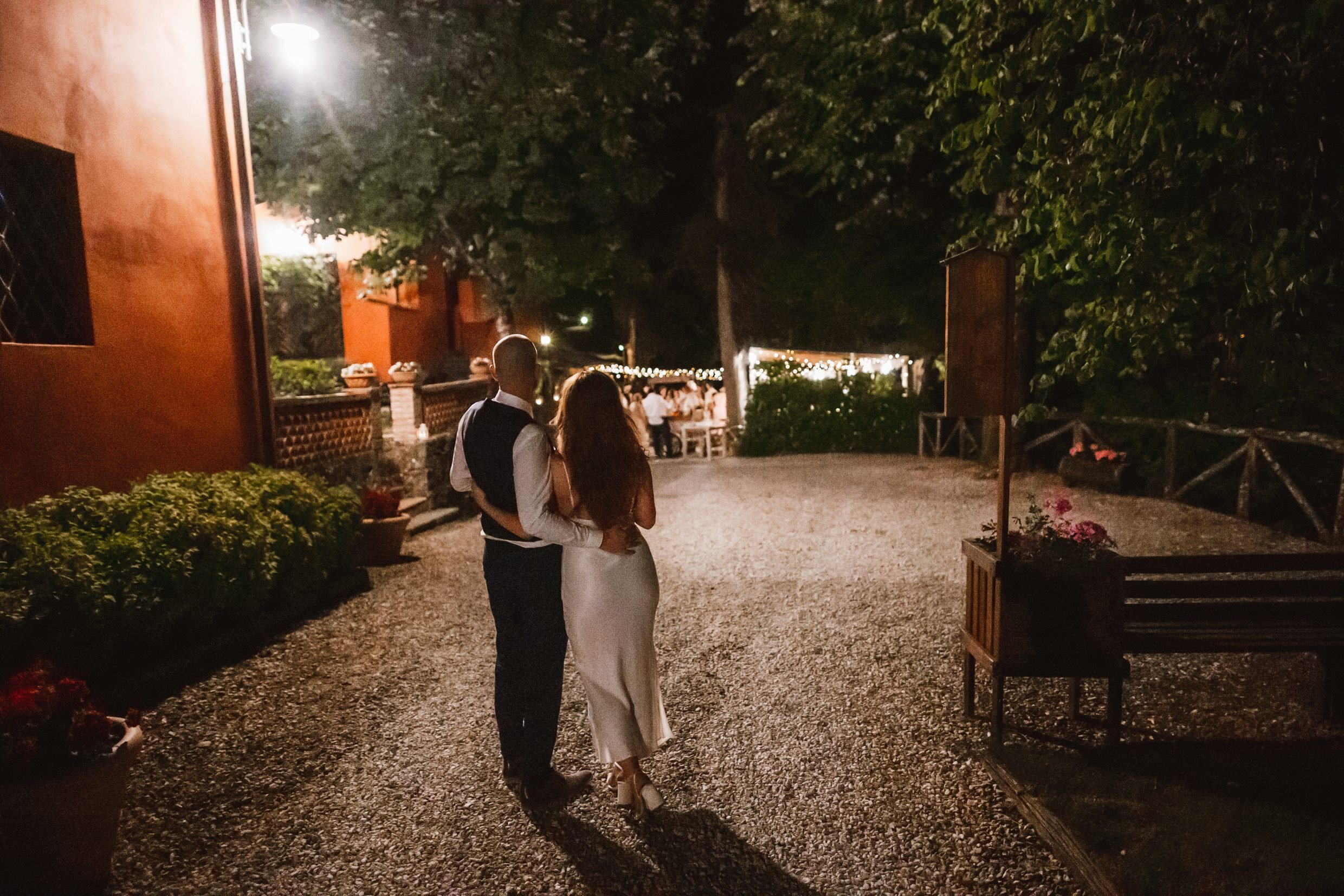 the bride and groom stand outside the villa at night looking towards the reception at the agriturismo la torre italian destination wedding venue in bagni di lucca tuscany