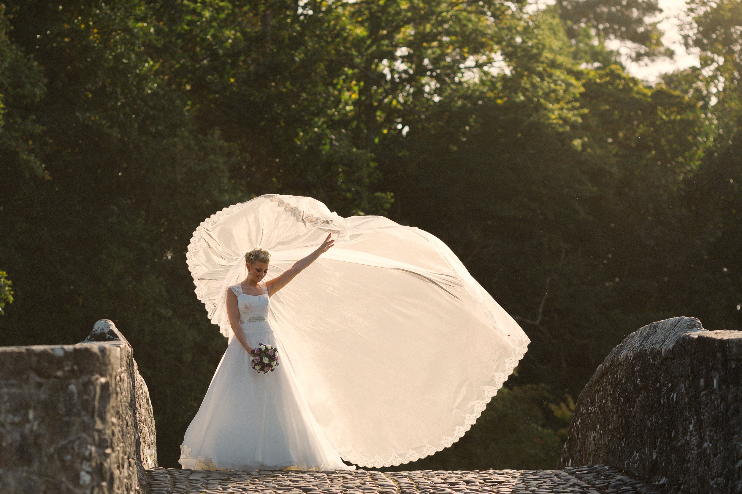  Bride stands on bride at brig o Doon with sun behind veil wedding photographer scotland prices 