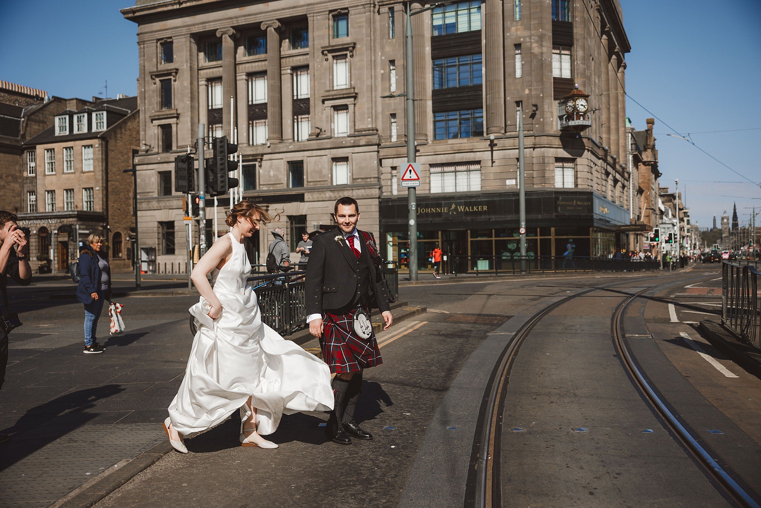 reportage photo of the bride and groom walking across princes street in edinburgh scotland by documentary wedding photographer edinburgh scotland