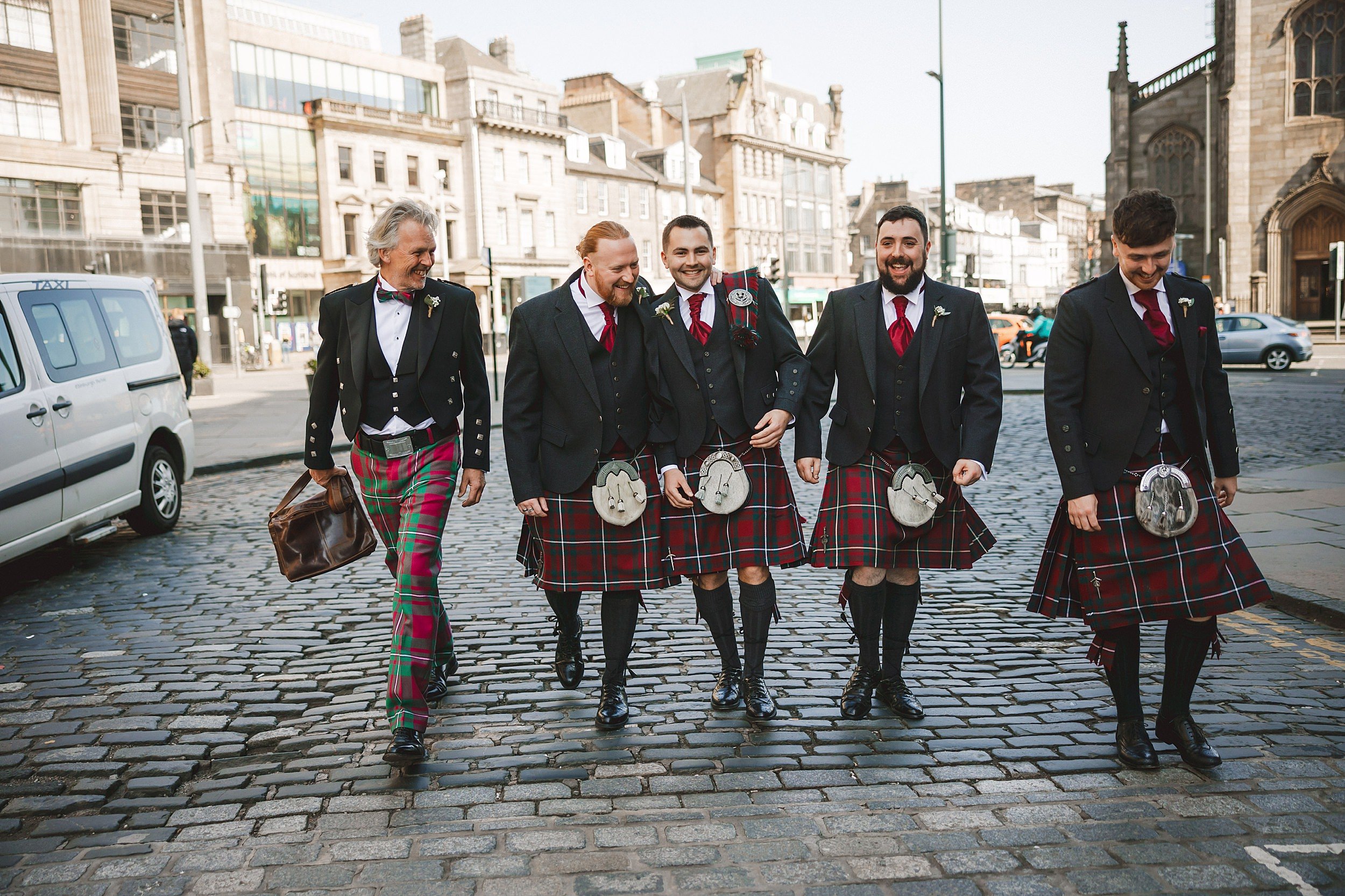 reportage photo of the groom and groomsmen wearing kilts walking along an Edinburgh street by documentary wedding photographer edinburgh scotland