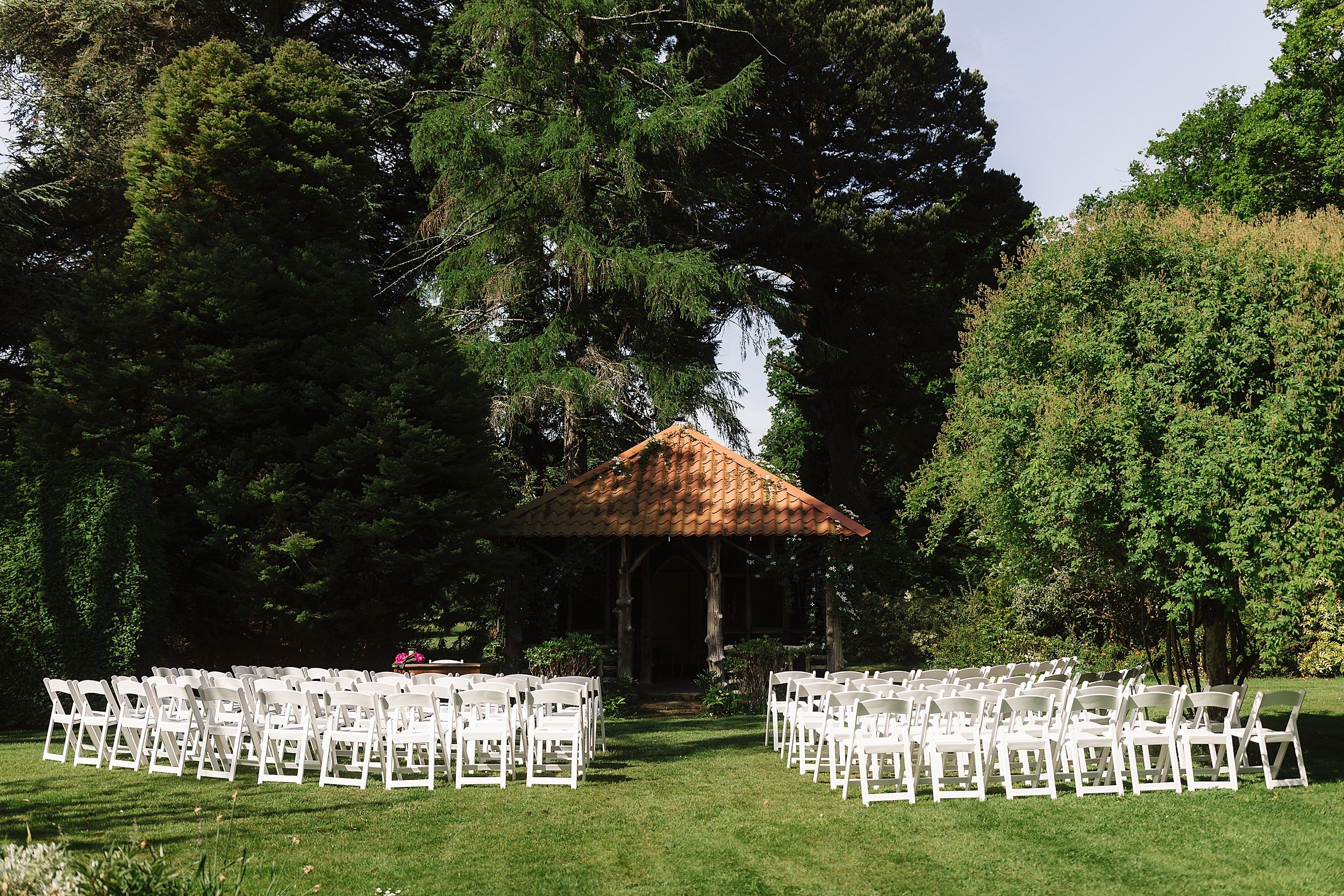 white chairs set up for a wedding ceremony in front of a wooden gazebo beneath trees in the gardens of errol park wedding venue in perthshire in scotland