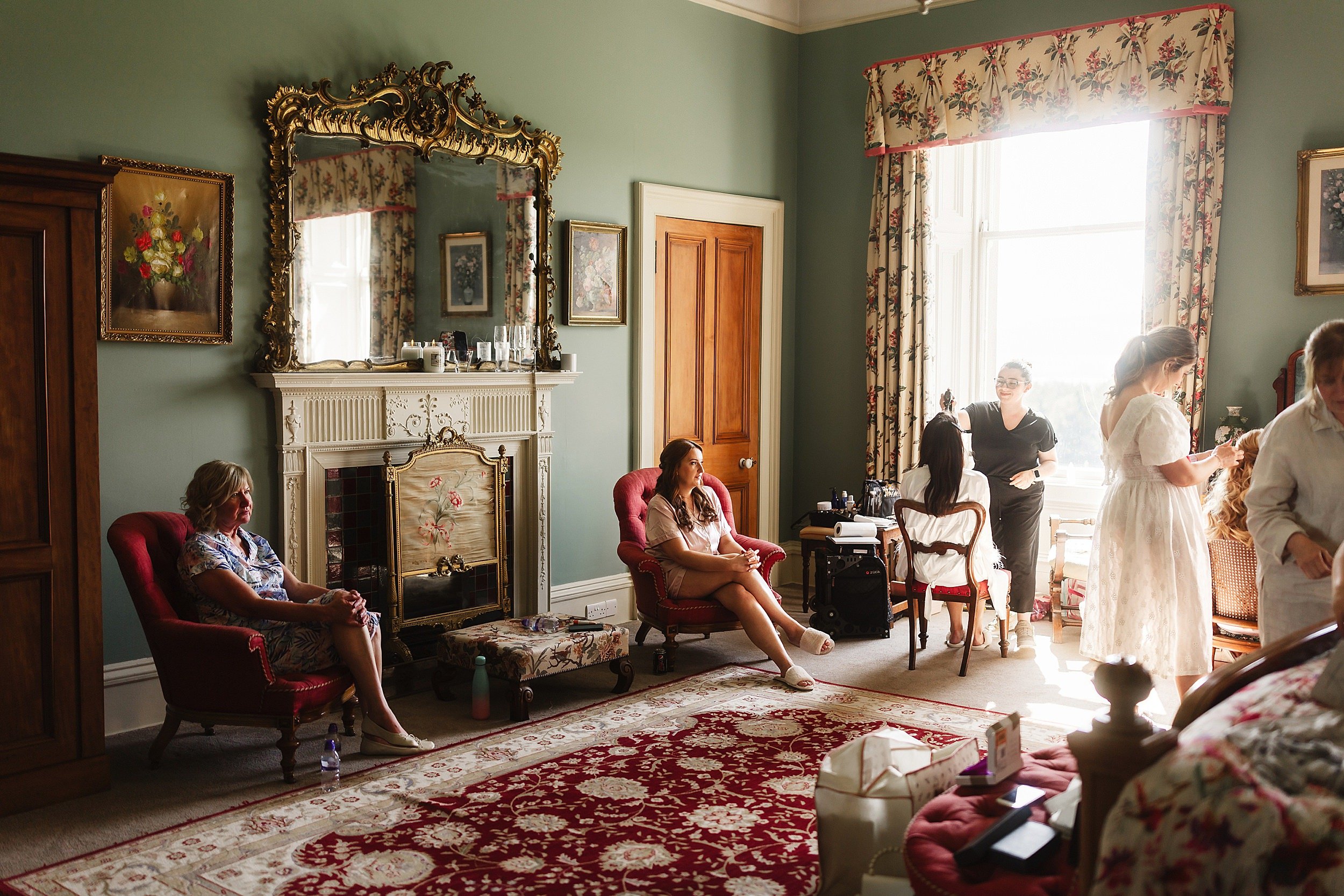 the bridal party preparing for the wedding ceremony in a bedroom with an ornate gold mirror above a fireplace in errol park wedding venue in perthshire scotland