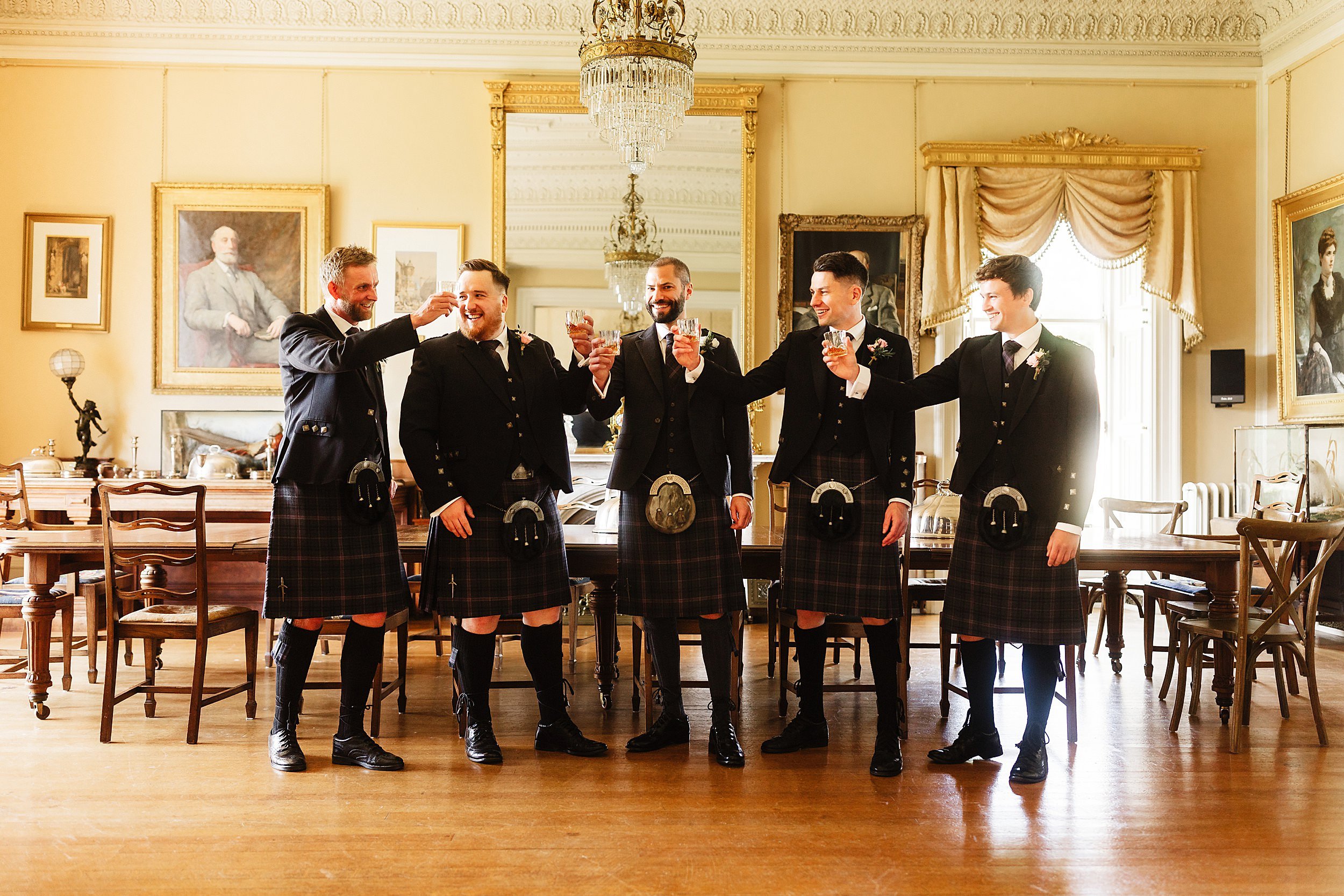 the groom and groomsmen raise their whisky glasses in an ornate dining room in errol park wedding venue in perthshire