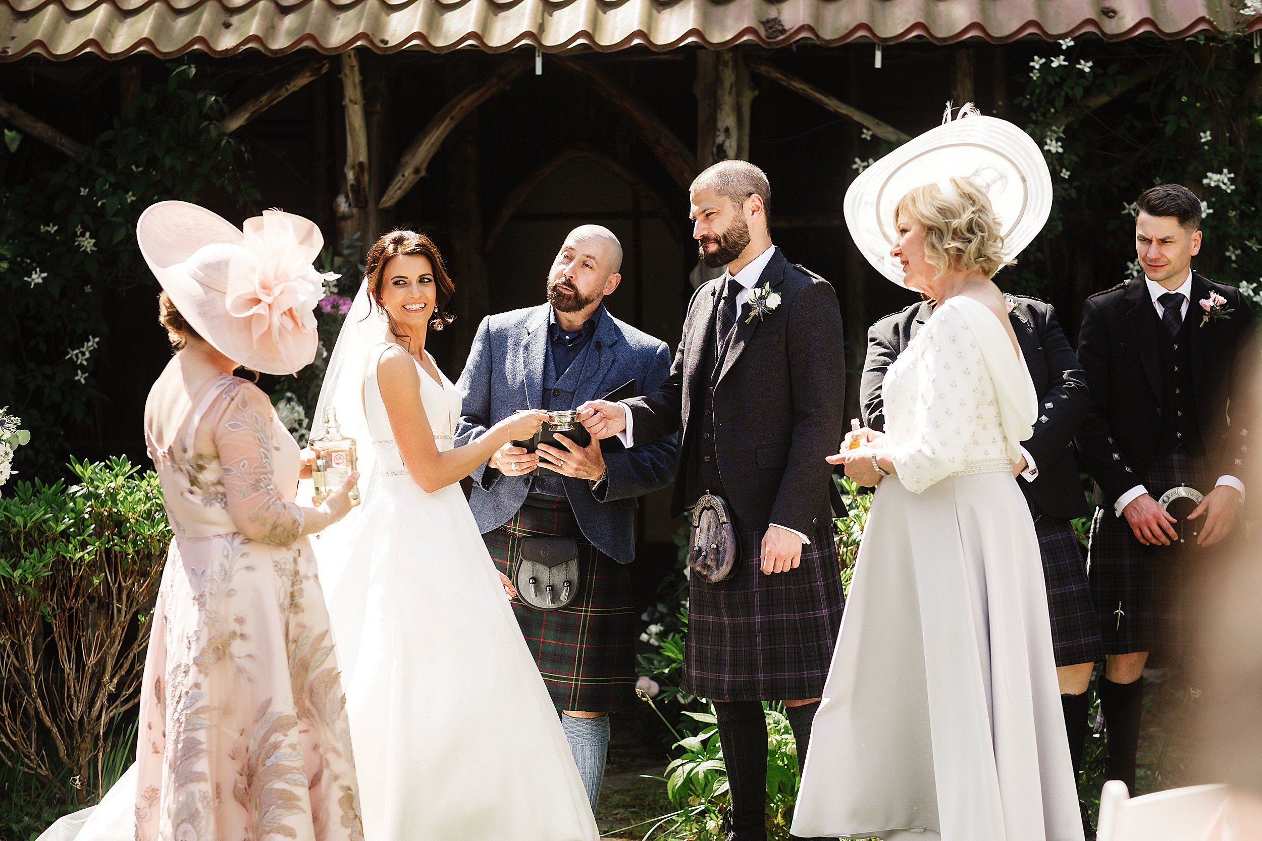 the bride and groom perform the quaich ceremony watched by their mothers during their wedding ceremony in the gardens of errol park wedding venue in perthshire in scotland 