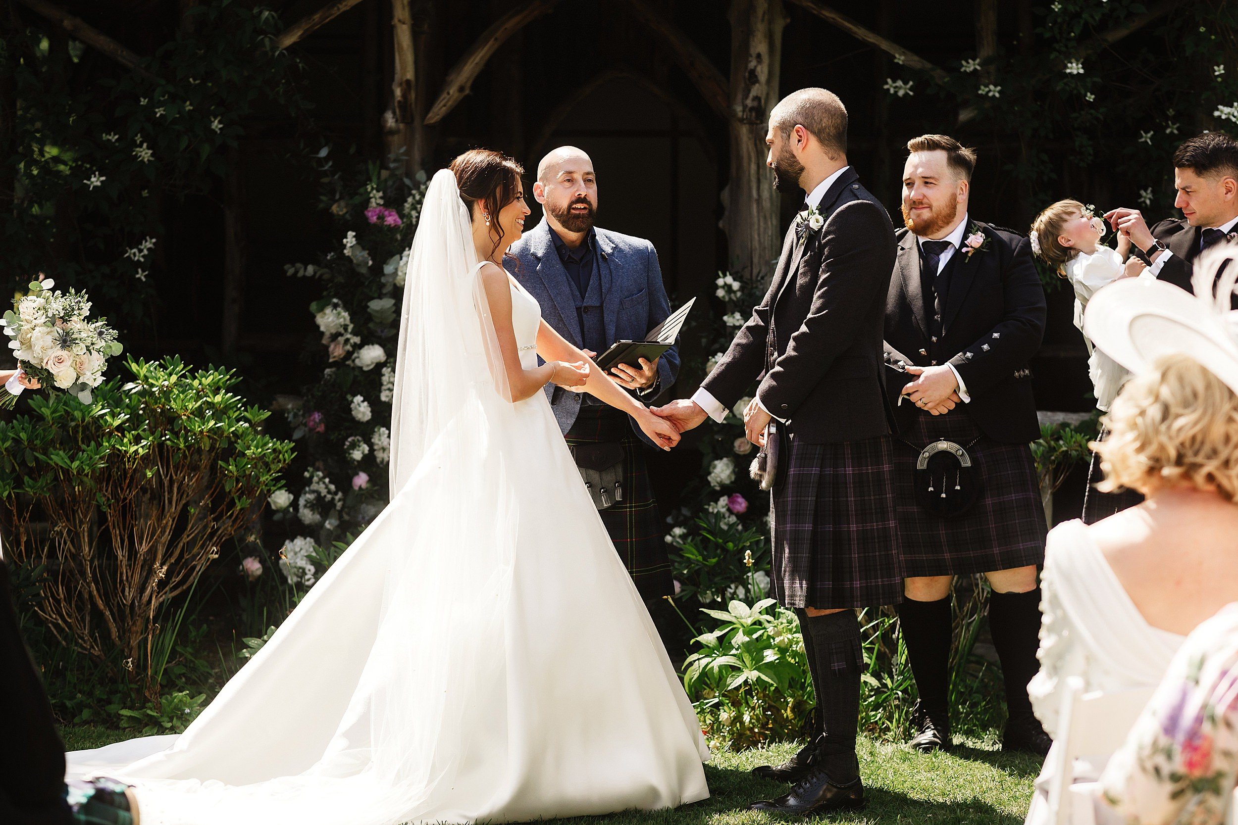 the bride and groom hold hands as the celebrant conducts their wedding ceremony in the gardens of errol park wedding venue in perthshire in scotland 