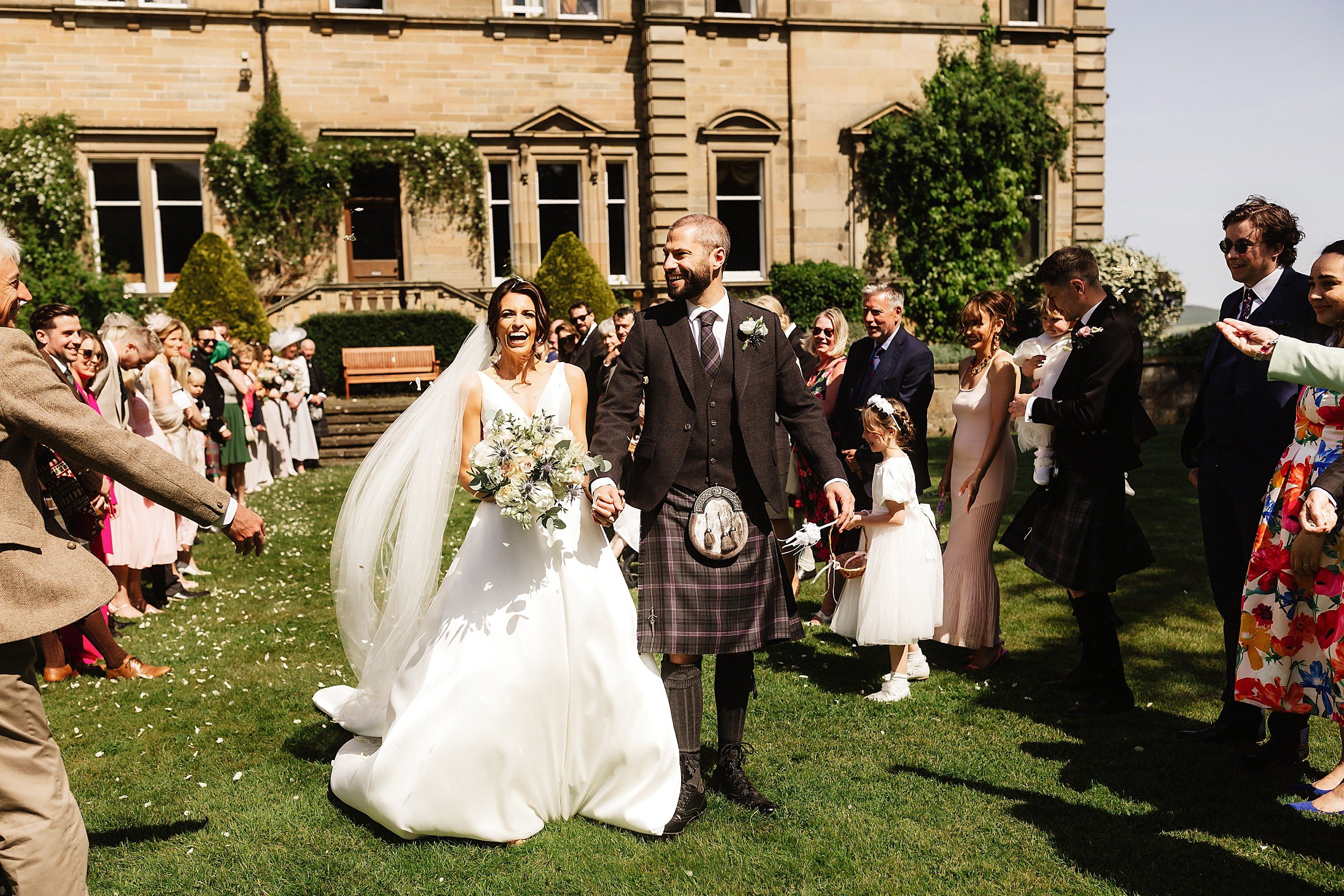 guests throw confetti as the bride and groom walk hand in hand away from errol park wedding venue stone steps and the house are visible behind them