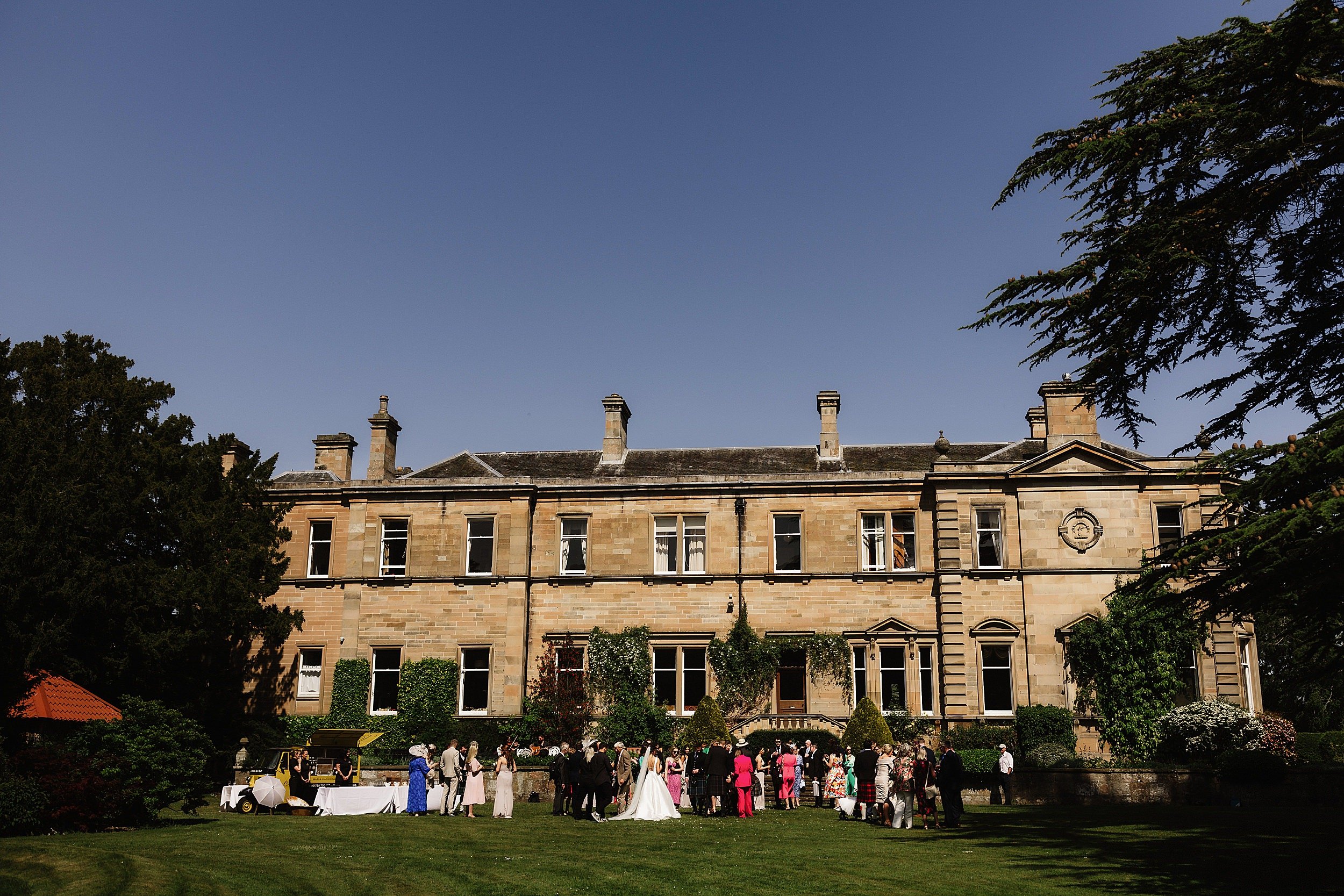 exterior outside view of errol park wedding venue with the bridal party and guests standing on the lawn 