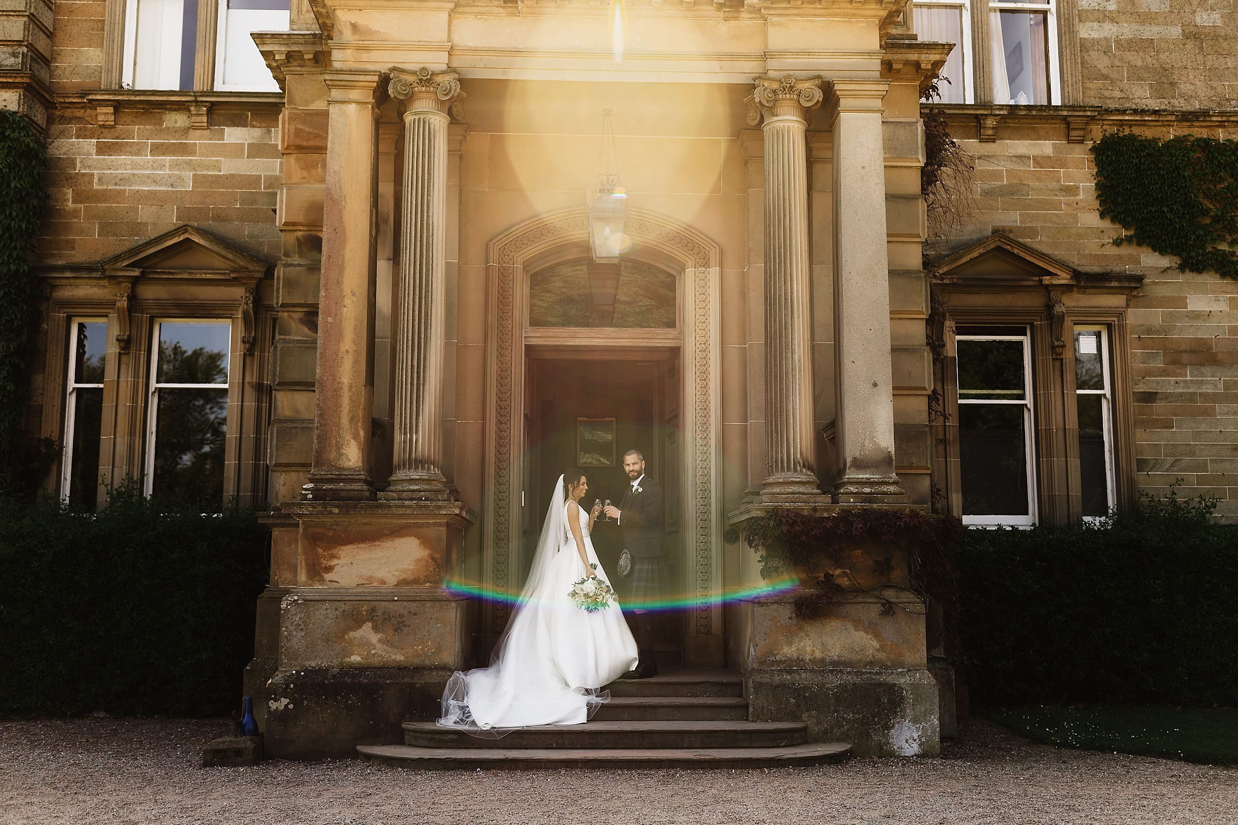 the bride and groom pose between stone pillars at the doorway of errol park wedding venue in perthshire scotland