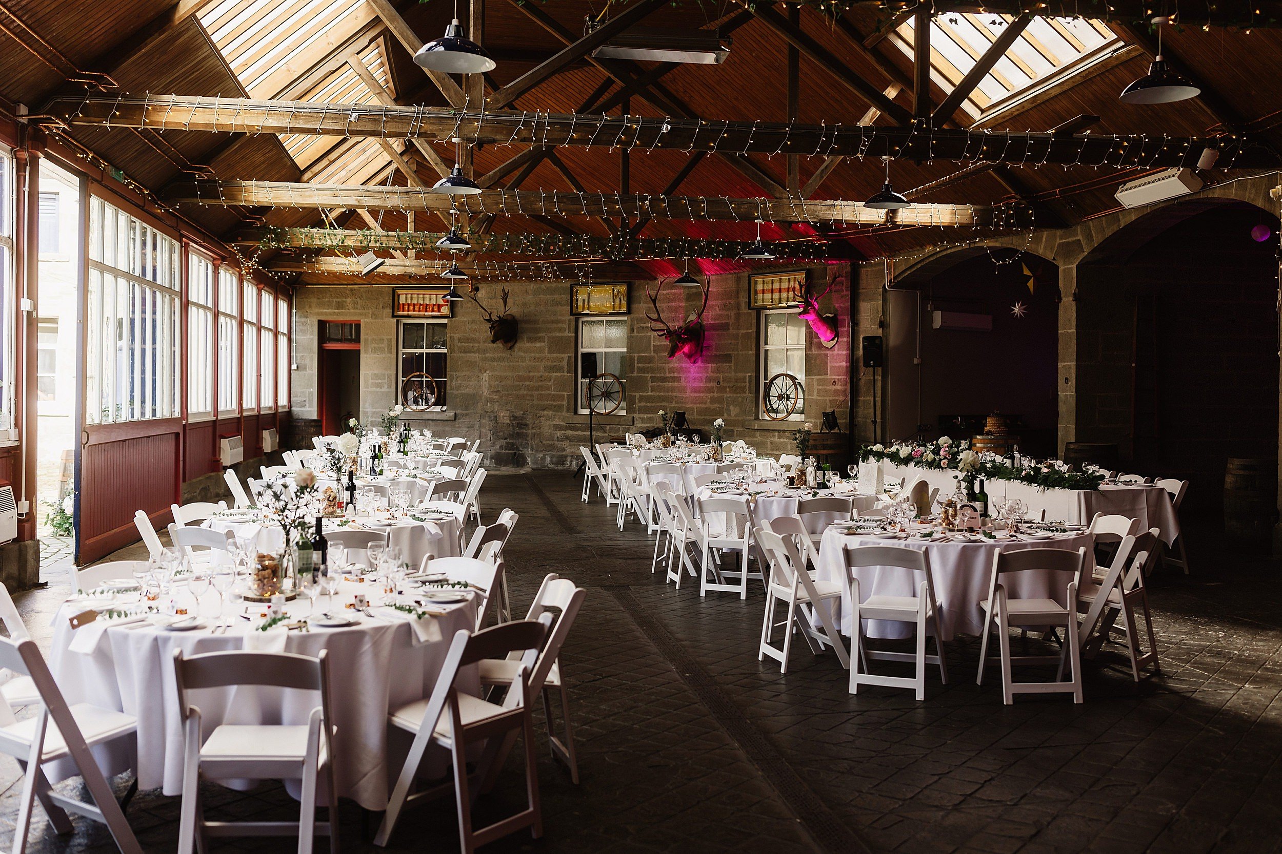 inside interior view of tables set for dinner in a room with a stone floor and beams with fairy lights in errol park wedding venue