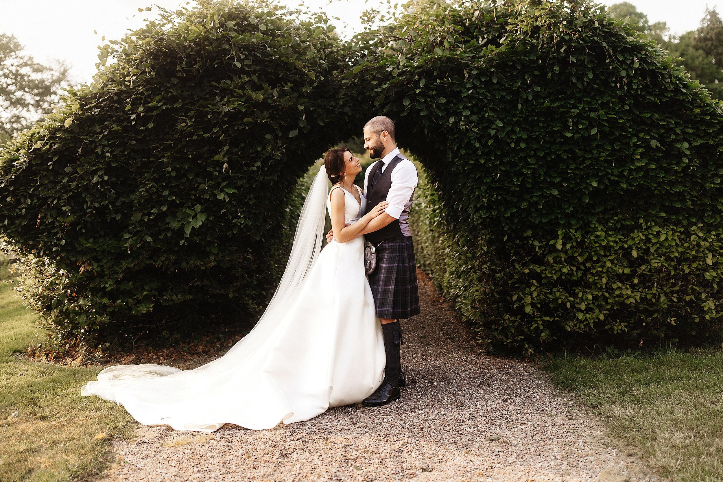 the bride and groom embrace in front of a topiary arch in the gardens of errol park wedding venue in perthshire in scotland