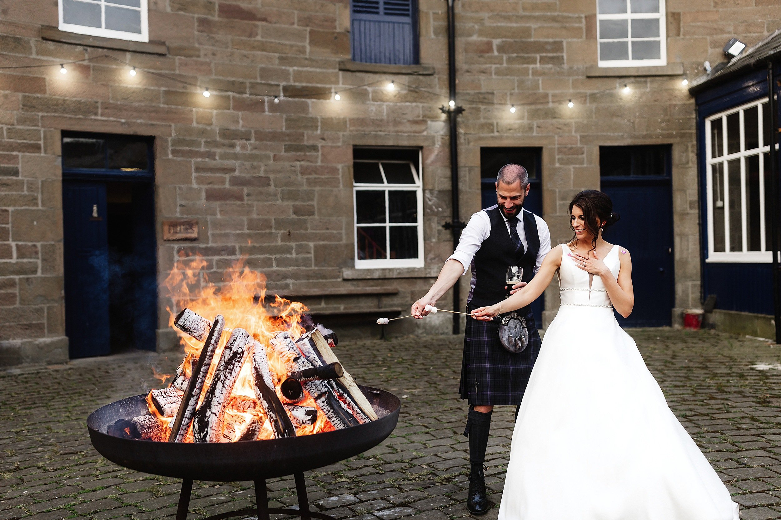 the bride and groom toast marshmallows at a brazier in the courtyard of errol park wedding venue in perthshire in scotland