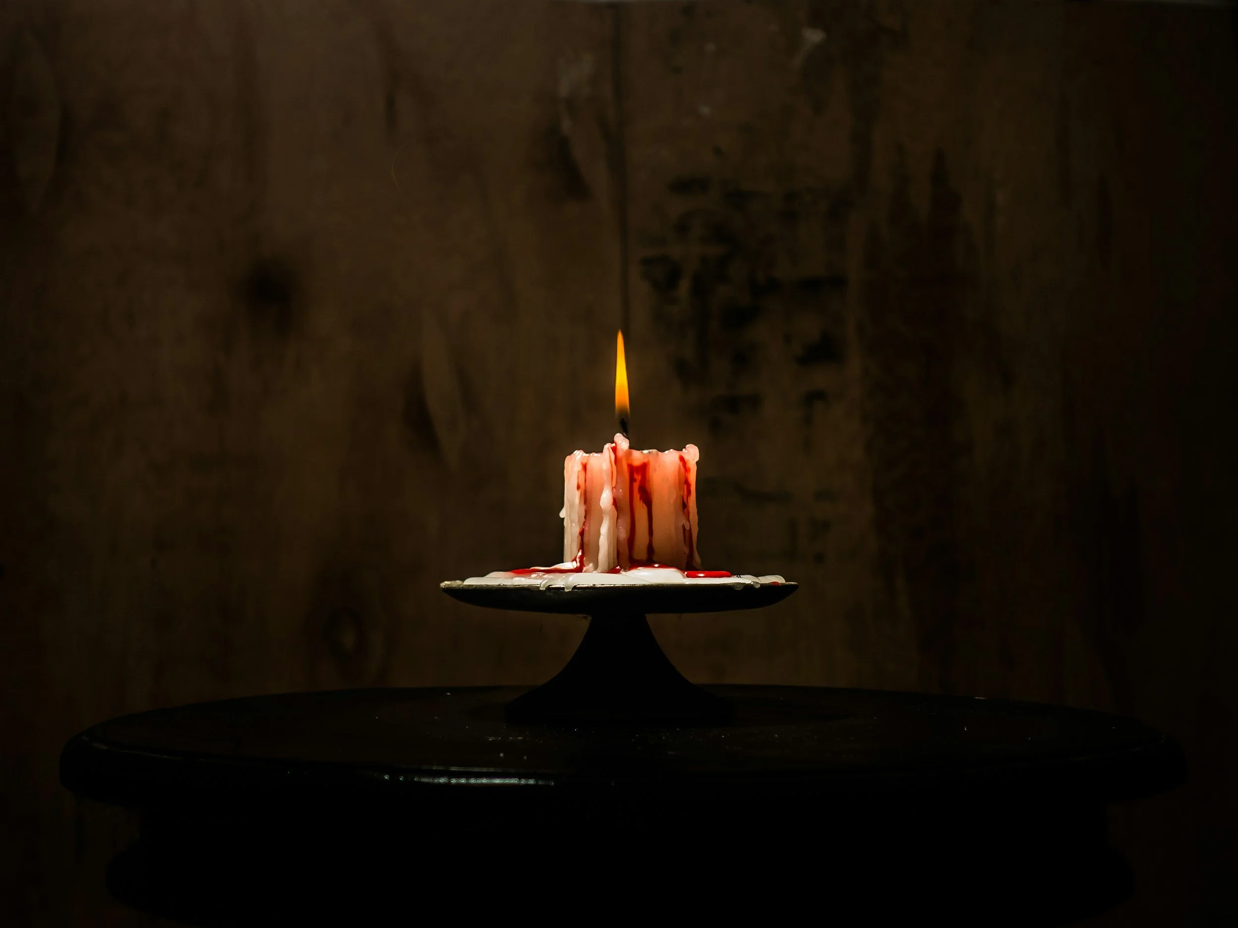 A single candle burning down against a dark red background