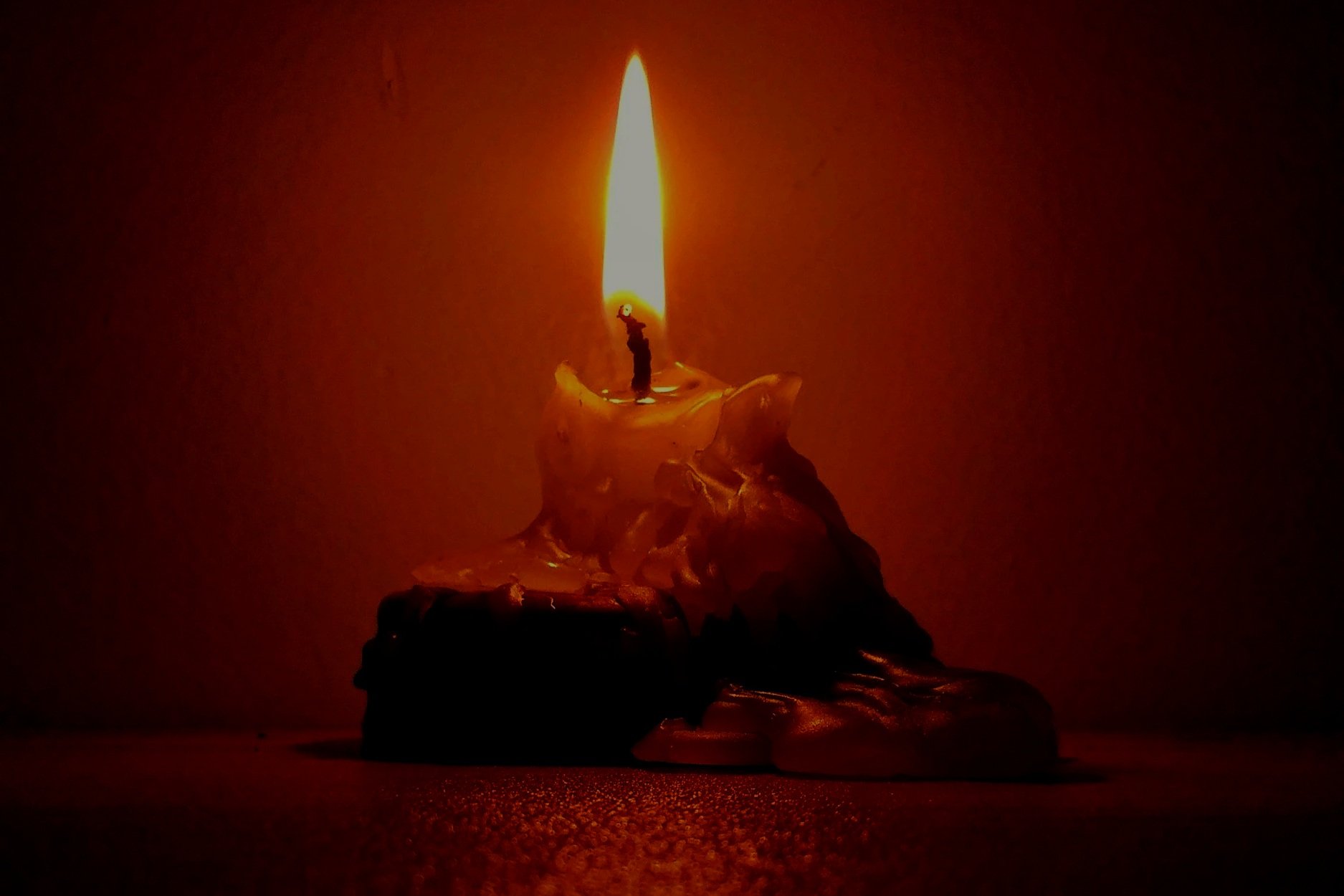 A single candle burning down against a dark red background