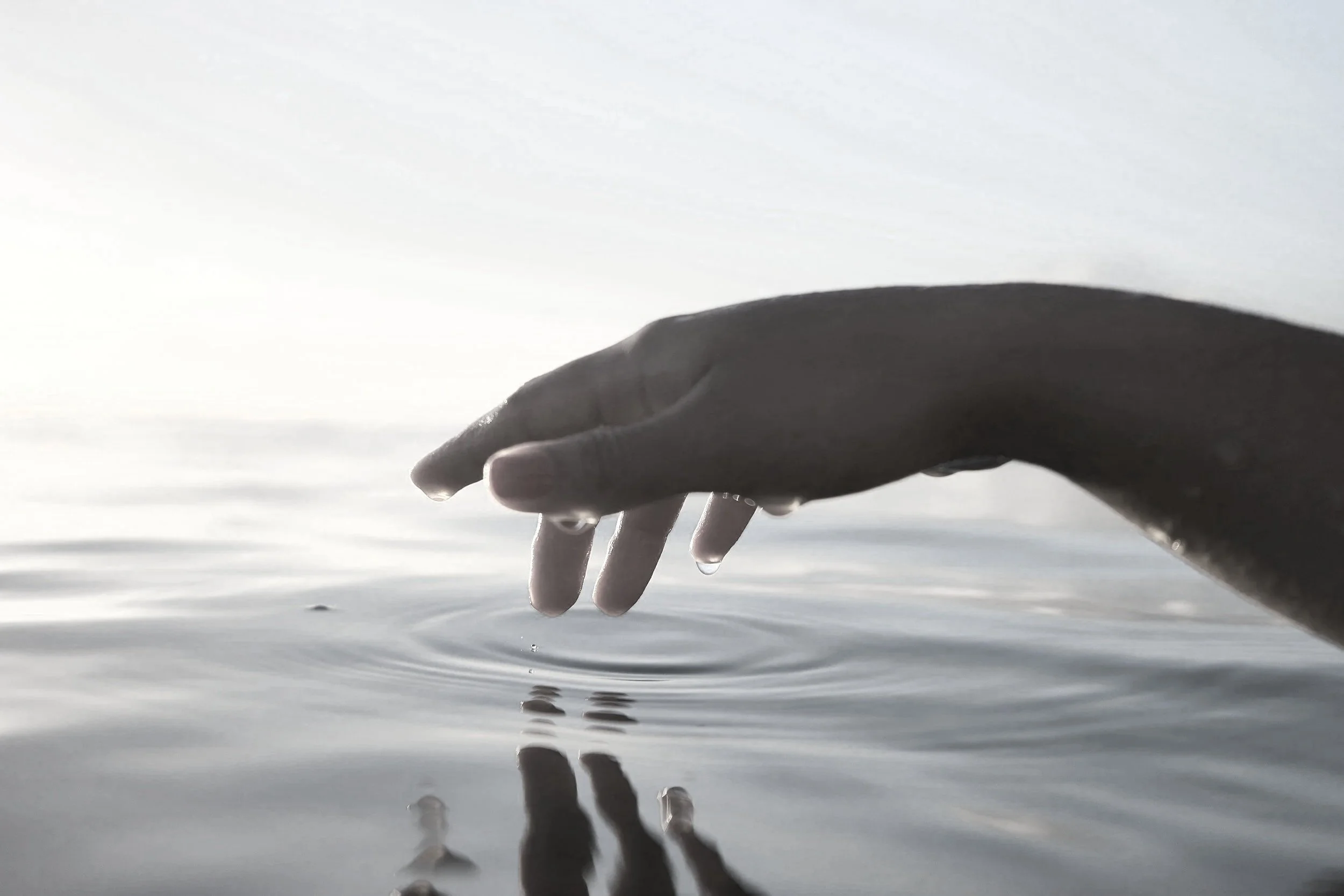 Fingertips touching calm water, creating gentle ripples across the surface