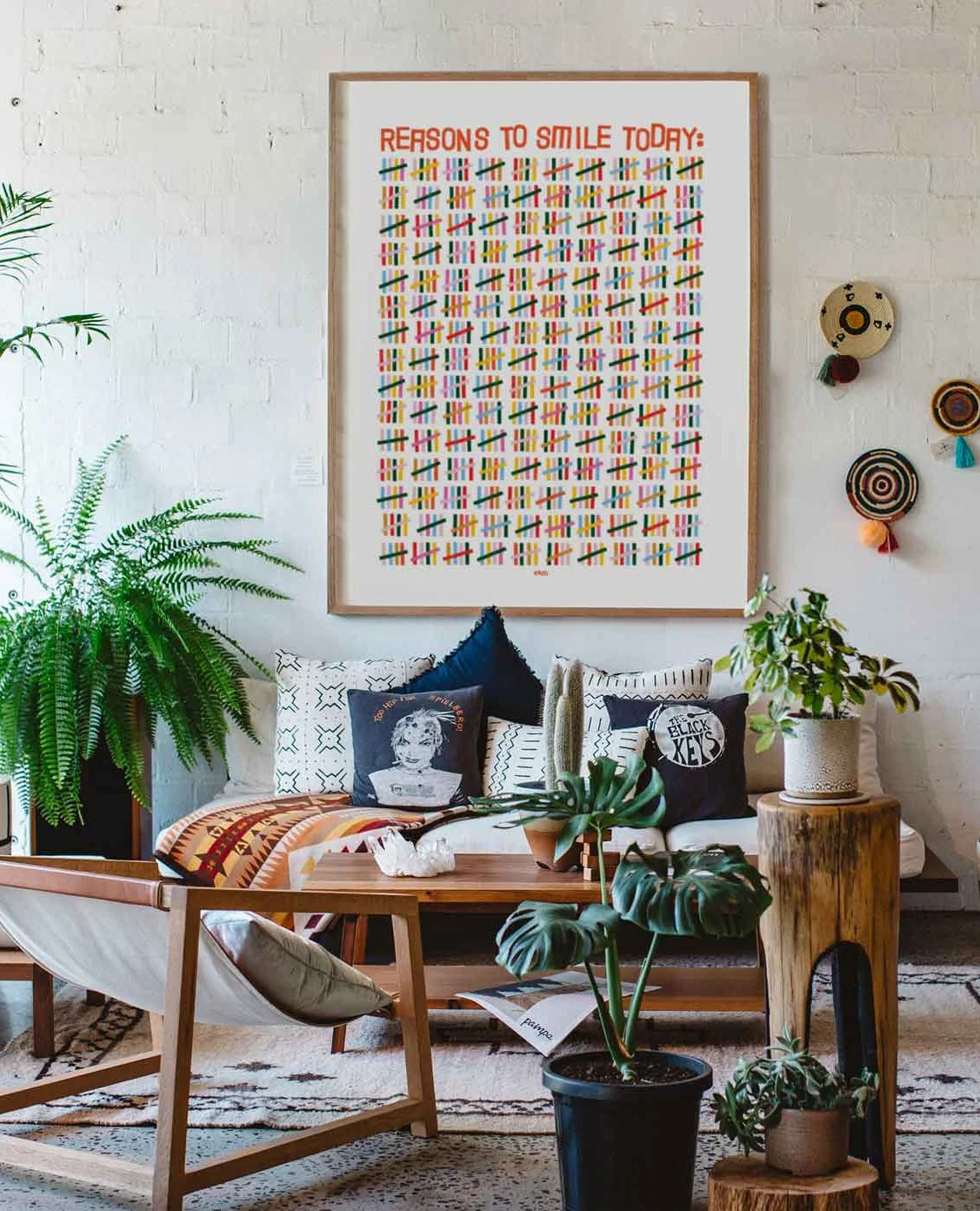 Boho living room with a white brick wall, large framed colorful quote poster, plants, pillows, a wooden coffee table, and decorative wall hangings.