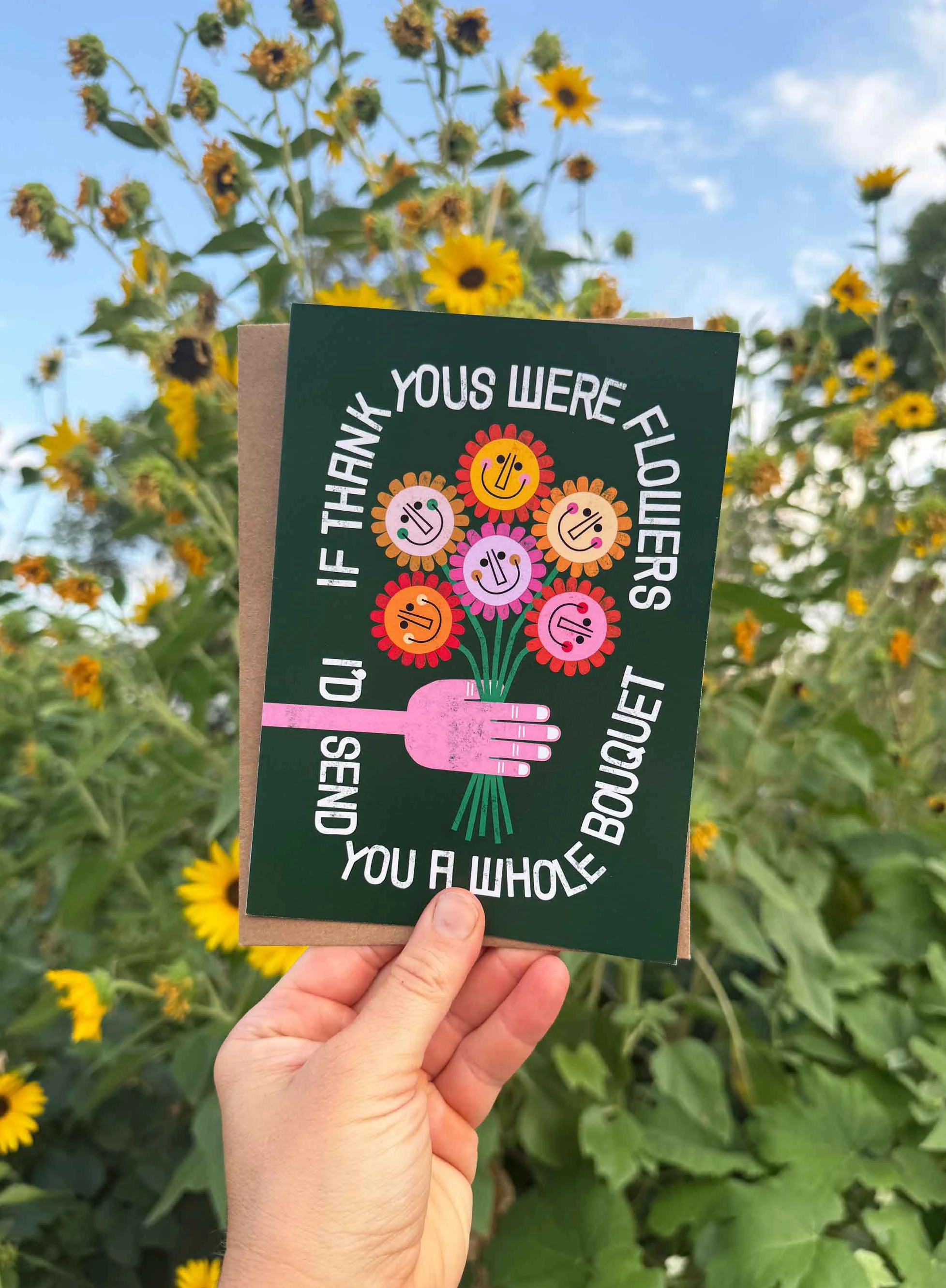 A person holding a bouquet of flowers card with the message, "If thank you were flowers I’d send you a whole bouquet," in front of a field of yellow sunflowers.