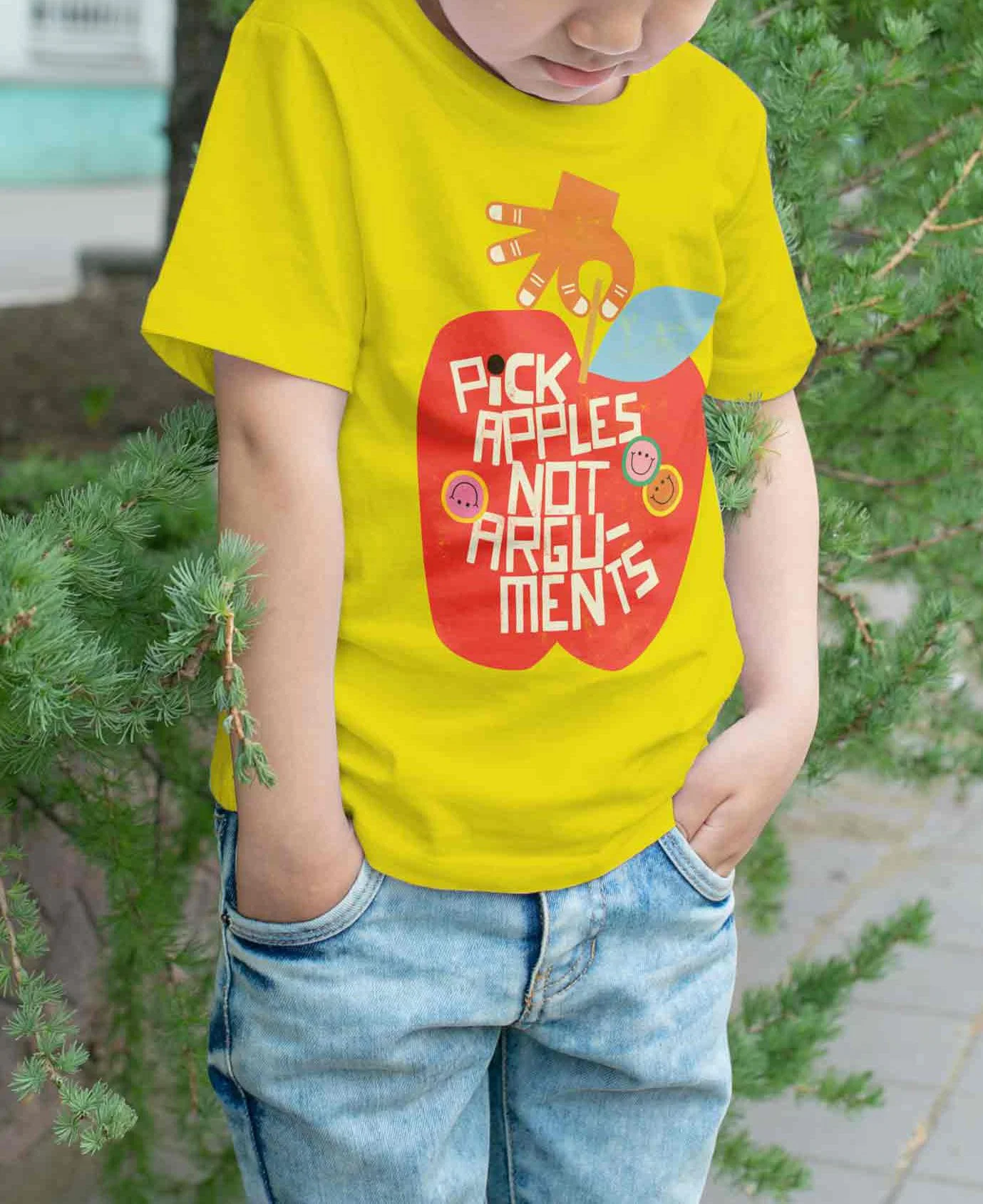 A person wearing a bright yellow T-shirt with a design of an apple and the words "Pick Apples Not Arguments" in red and white lettering, standing outdoors near green foliage.