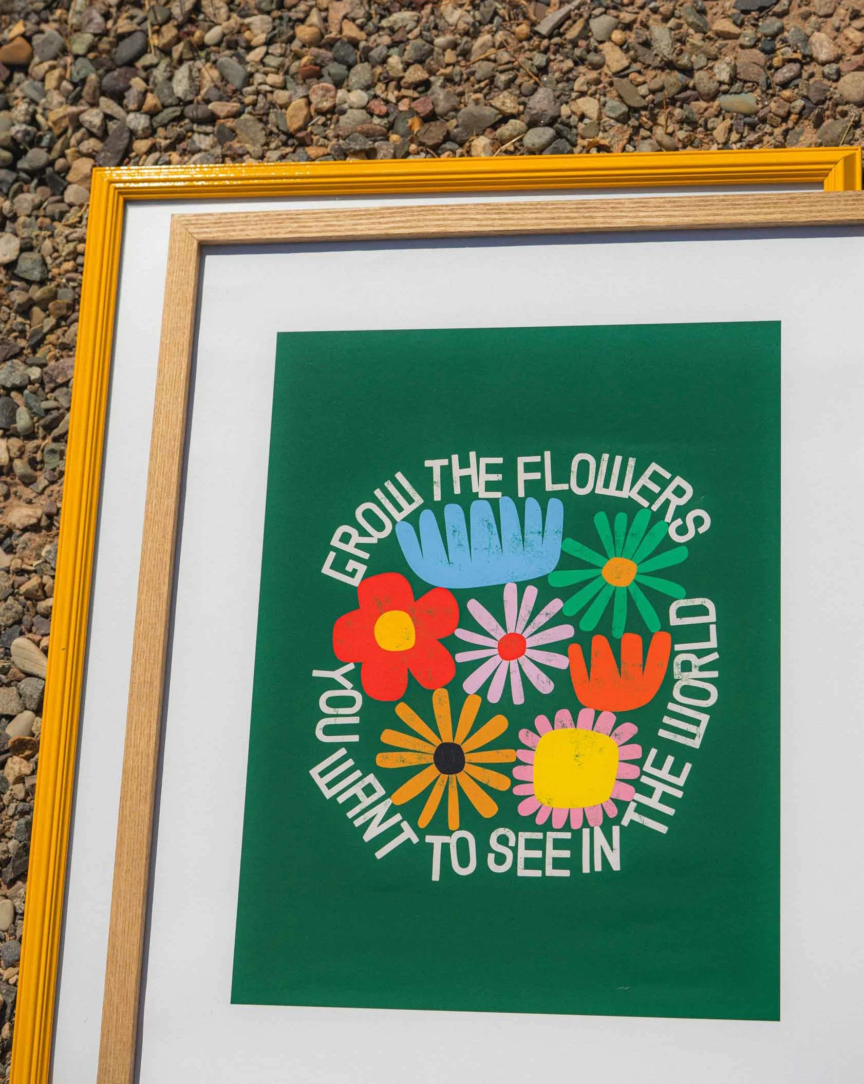 Colorful illustration of various flowers with the quote 'GROW THE FLOWERS YOU WANT TO SEE IN THE WORLD' in white text around the flowers, set on a green background with yellow, blue, red, pink, orange, and black elements.