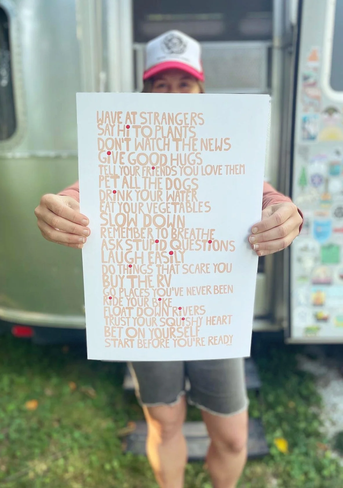 Person holding a piece of paper with a list of positive and adventurous suggestions, standing outdoors with Airstream background.