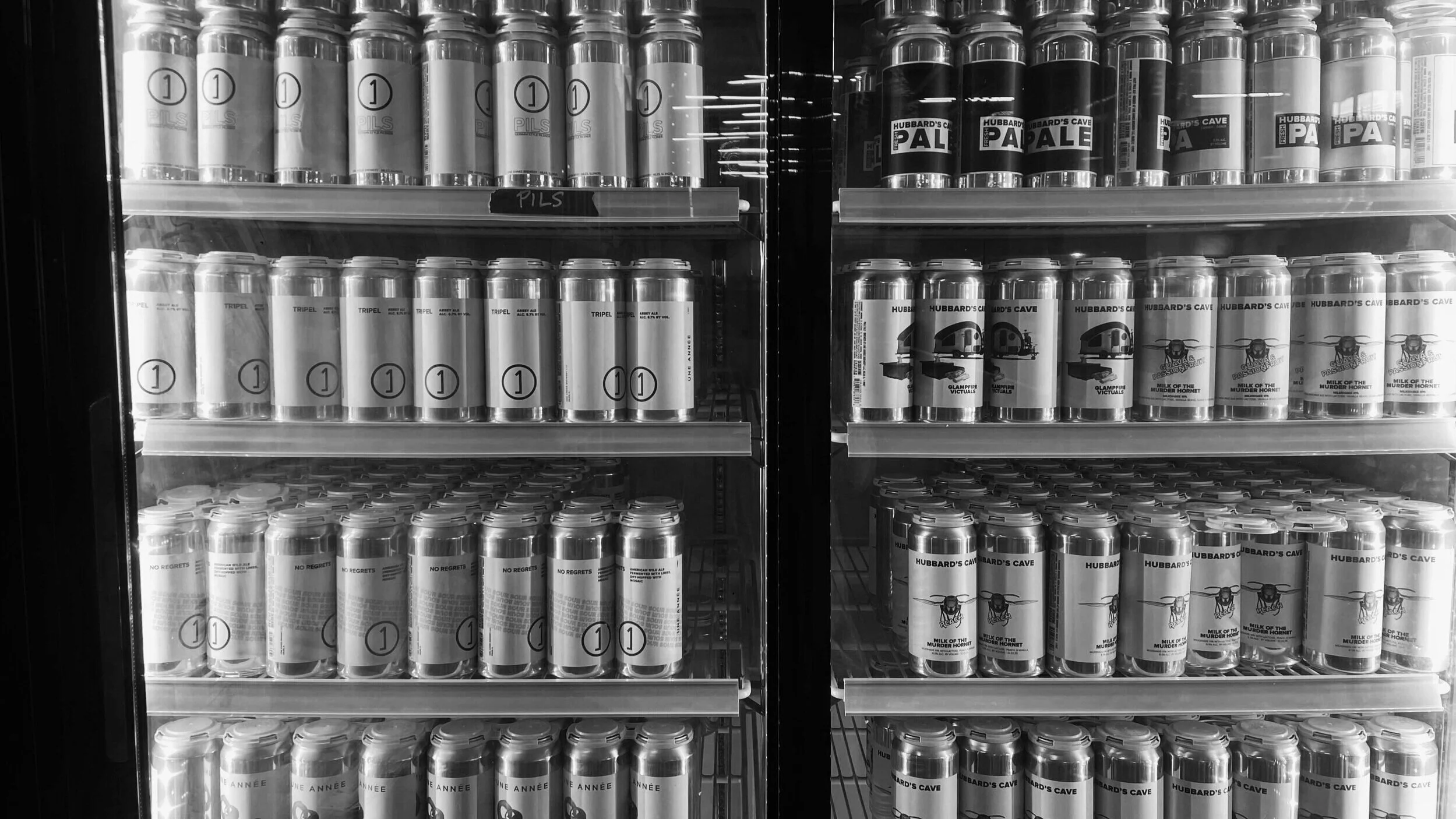 Refrigerated display case with rows of canned and bottled craft beers.