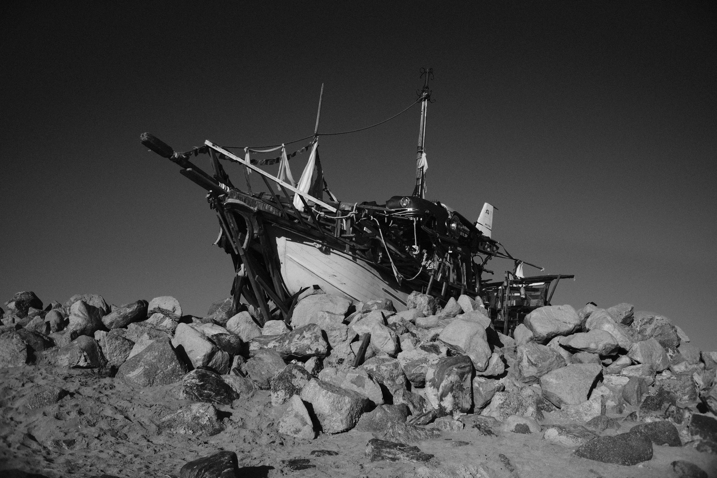 A wrecked boat sitting on a rocky shore under a clear sky.