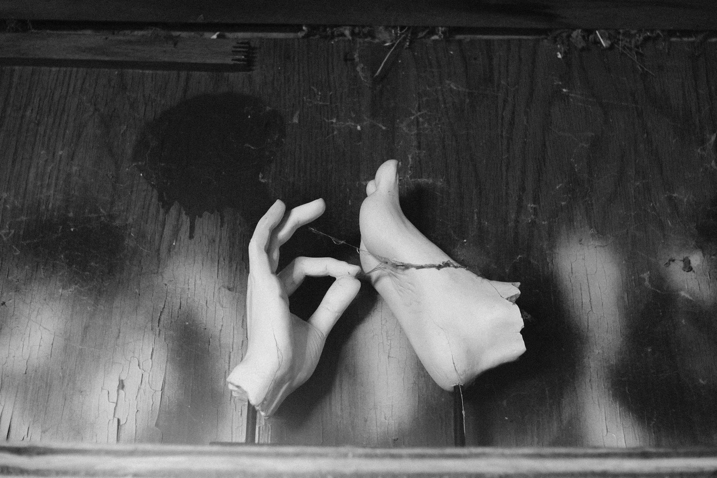 Black and white photo of a mannequin's hand resting on a wooden surface, with a fragment of a broken ceramic figure nearby, viewed from above.