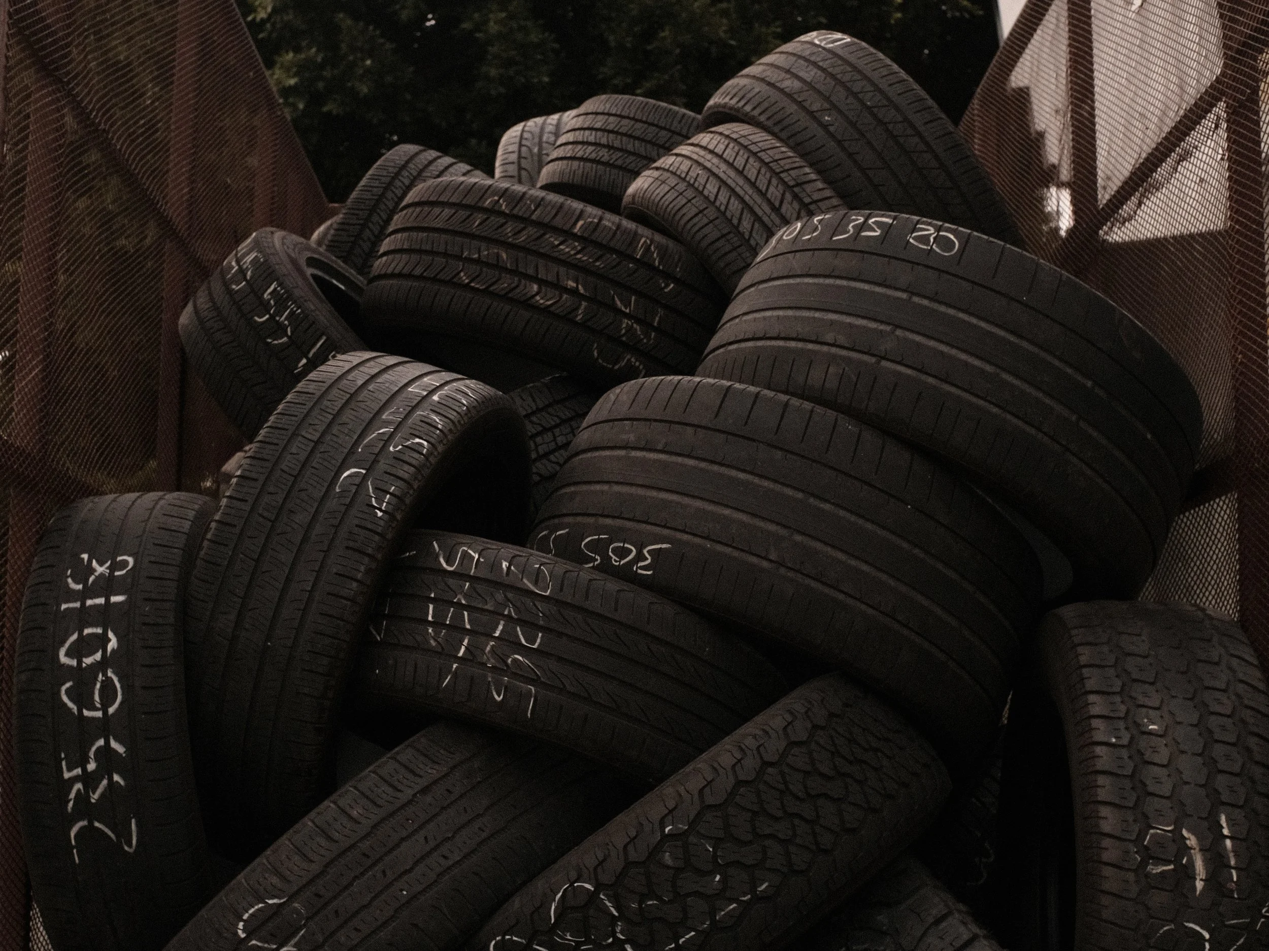 A pile of used car tires stacked inside a mesh-sided trailer or storage container.