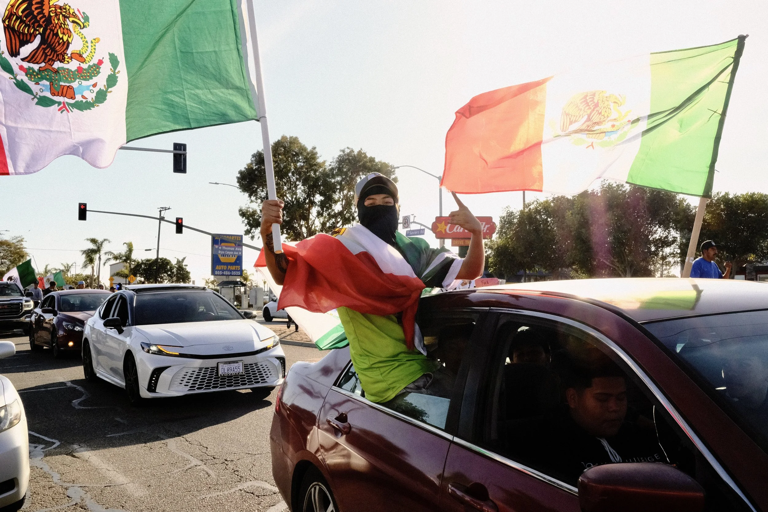 Person standing in a car with Mexican flags waving on either side during a parade or celebration.